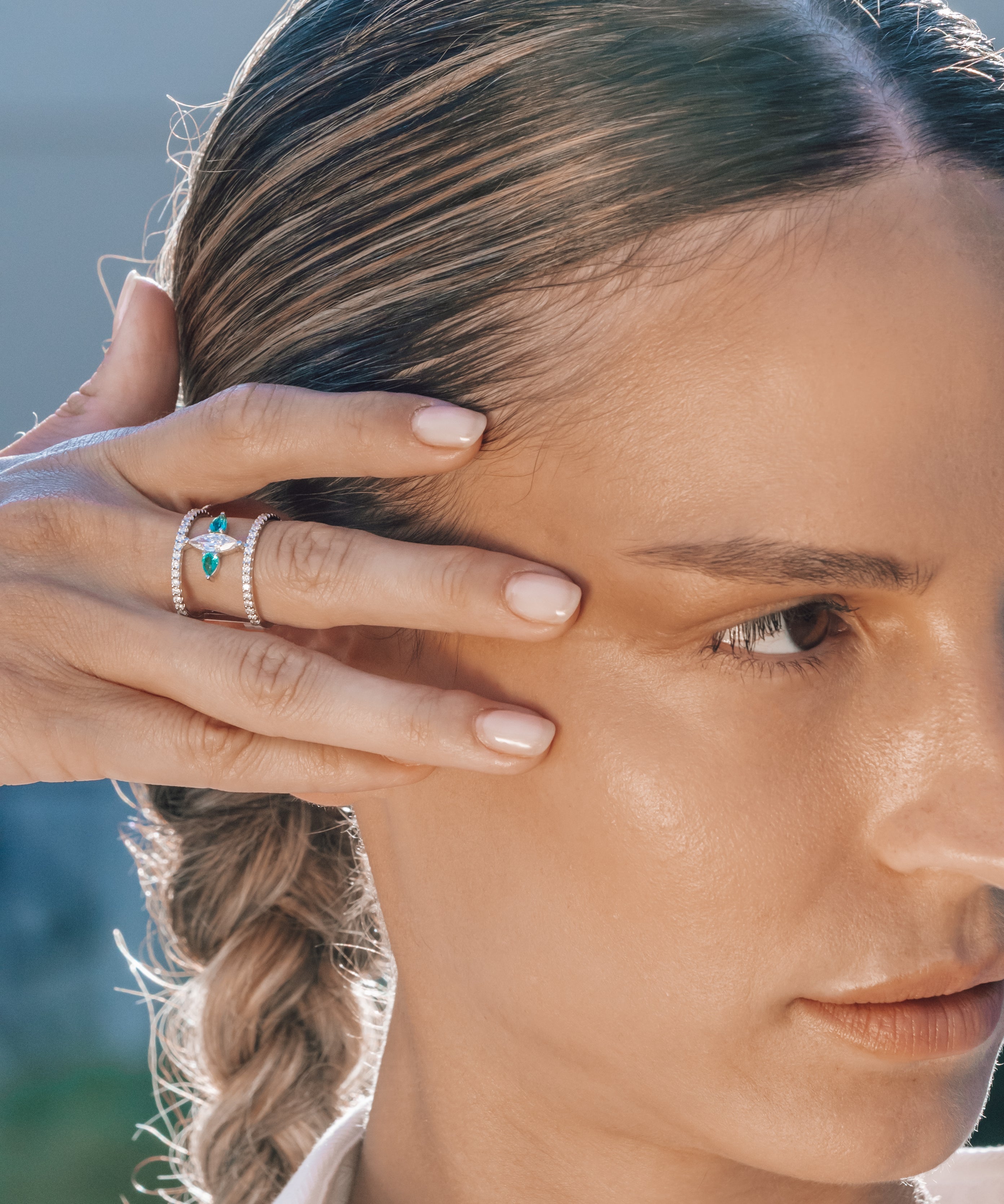 Close-up of a woman with braided hair wearing a special emerald ring and a blurred natural background