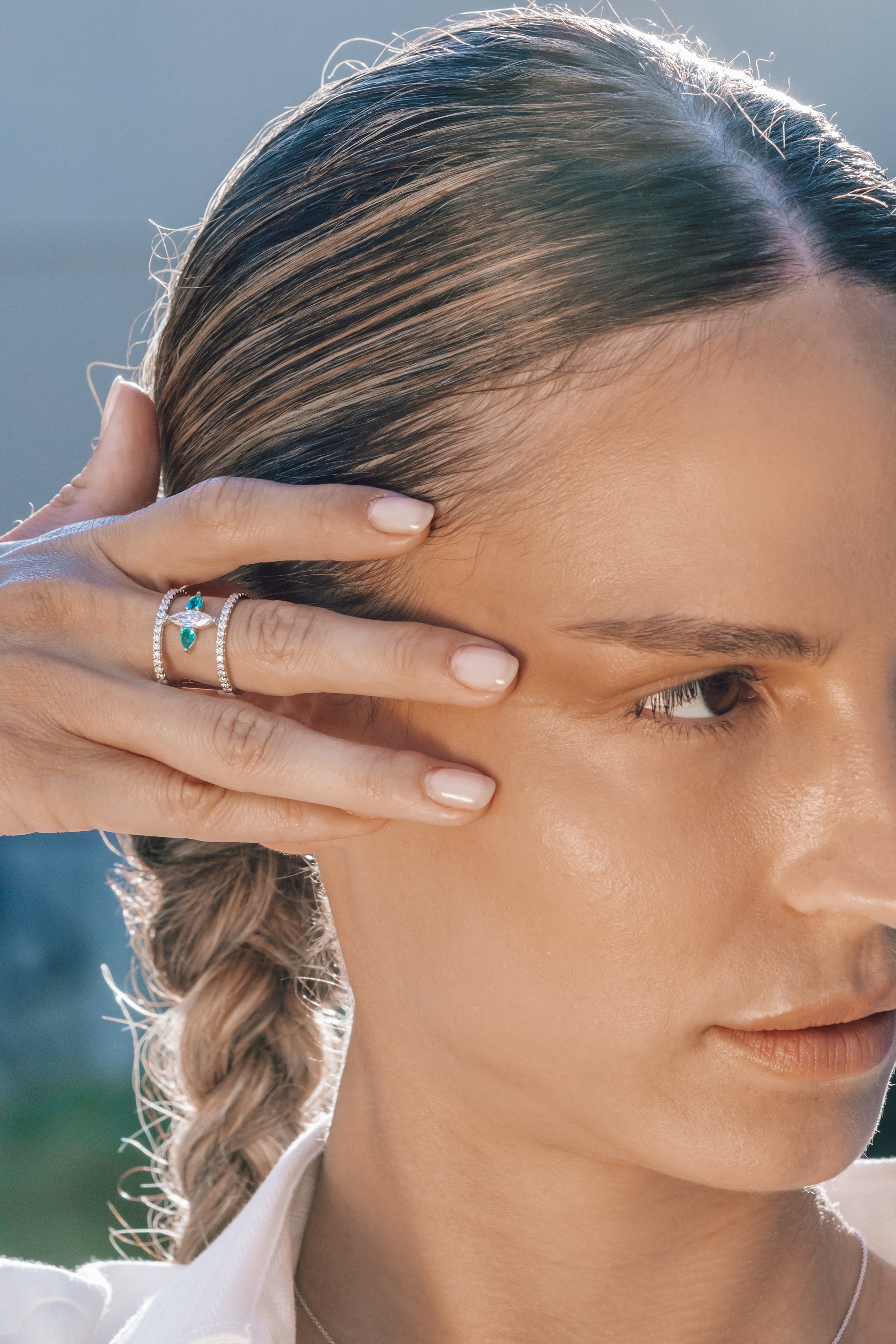 Close-up of a woman with braided hair wearing a special emerald ring and a blurred natural background