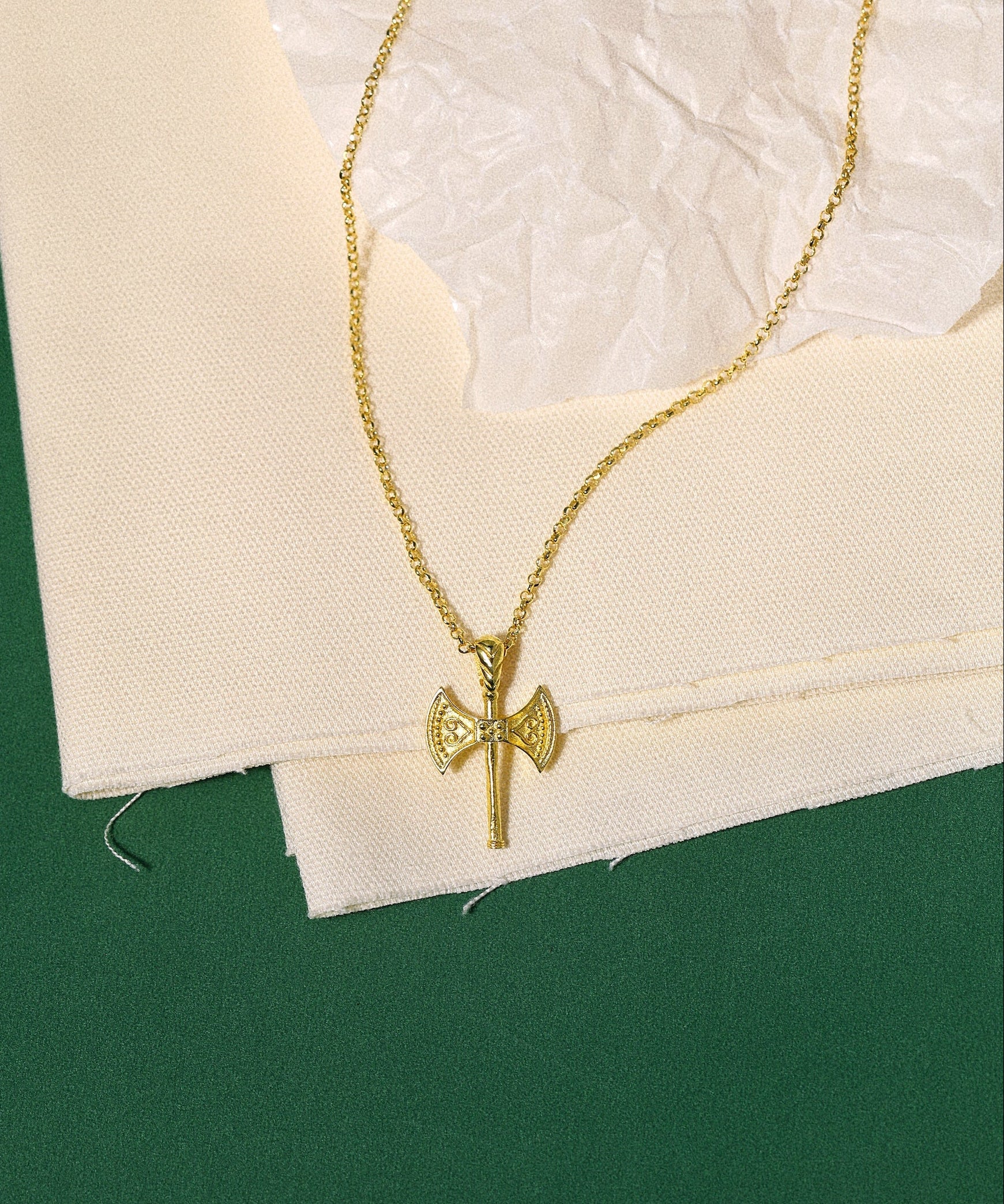 Gold necklace with a axe pendant on a textured white surface