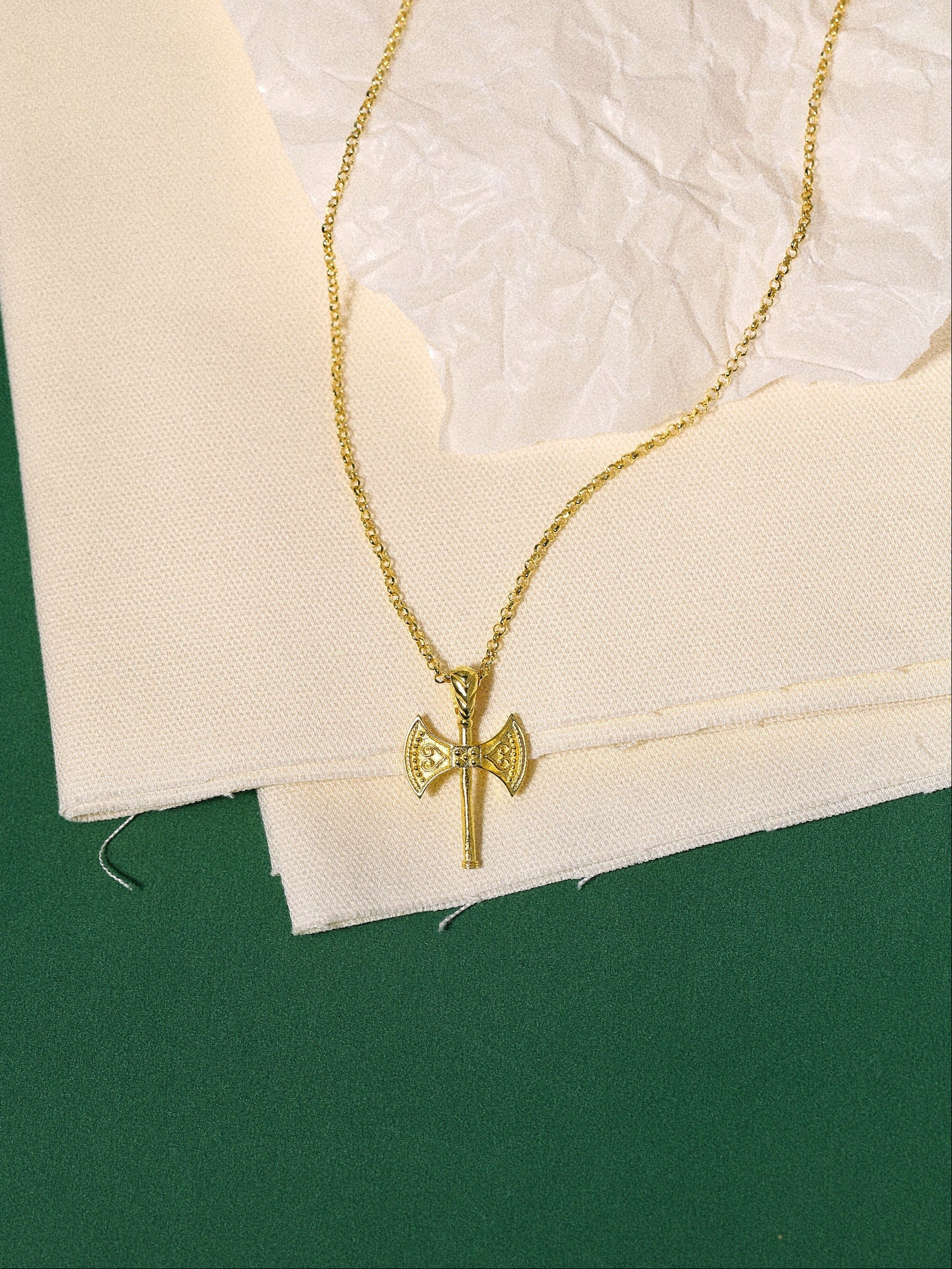 Gold necklace with a axe pendant on a textured white surface