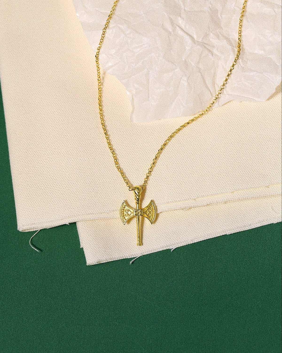 Gold necklace with a axe pendant on a textured white surface