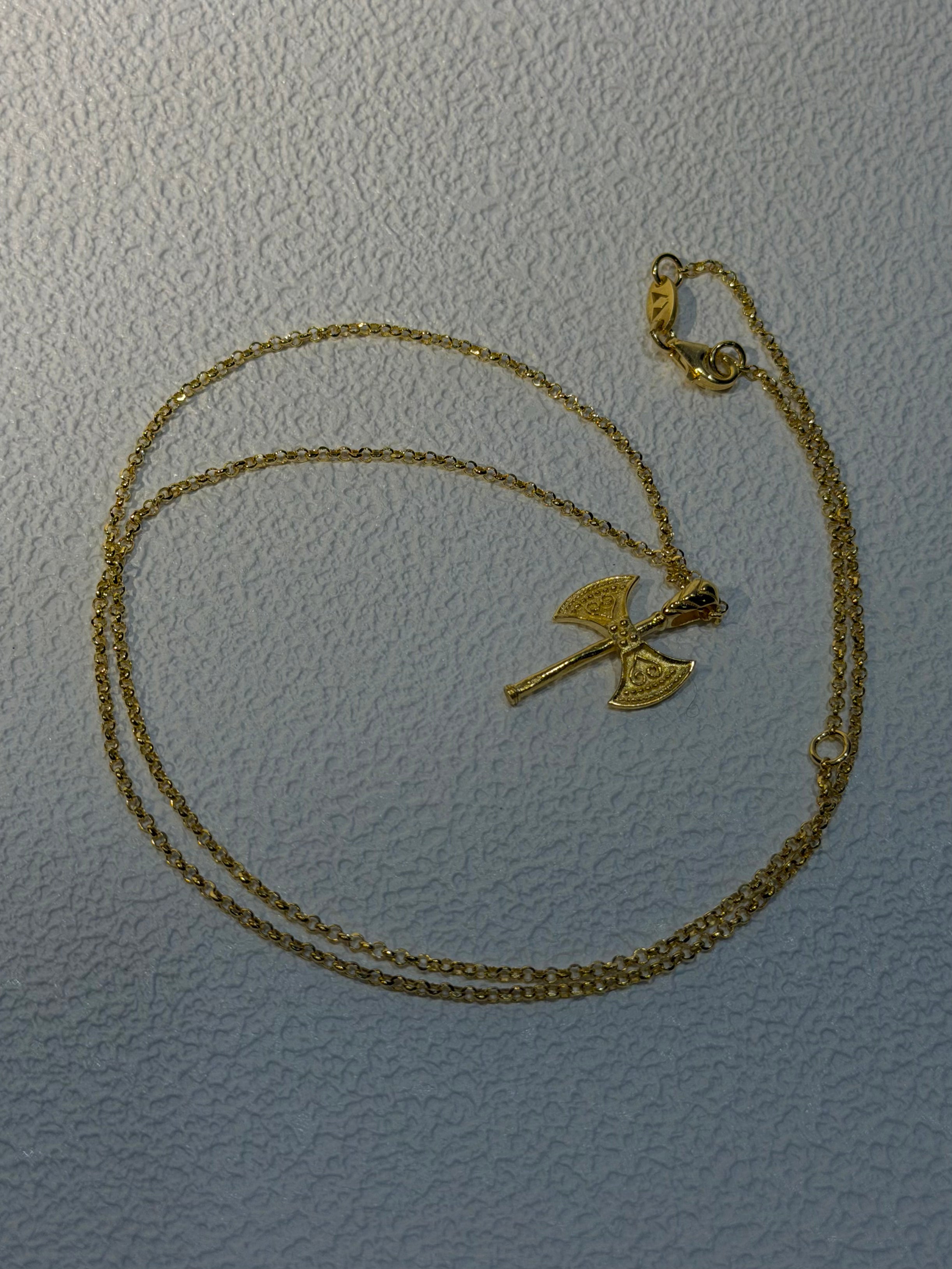 Gold necklace with a unique double-axe pendant on a light gray background