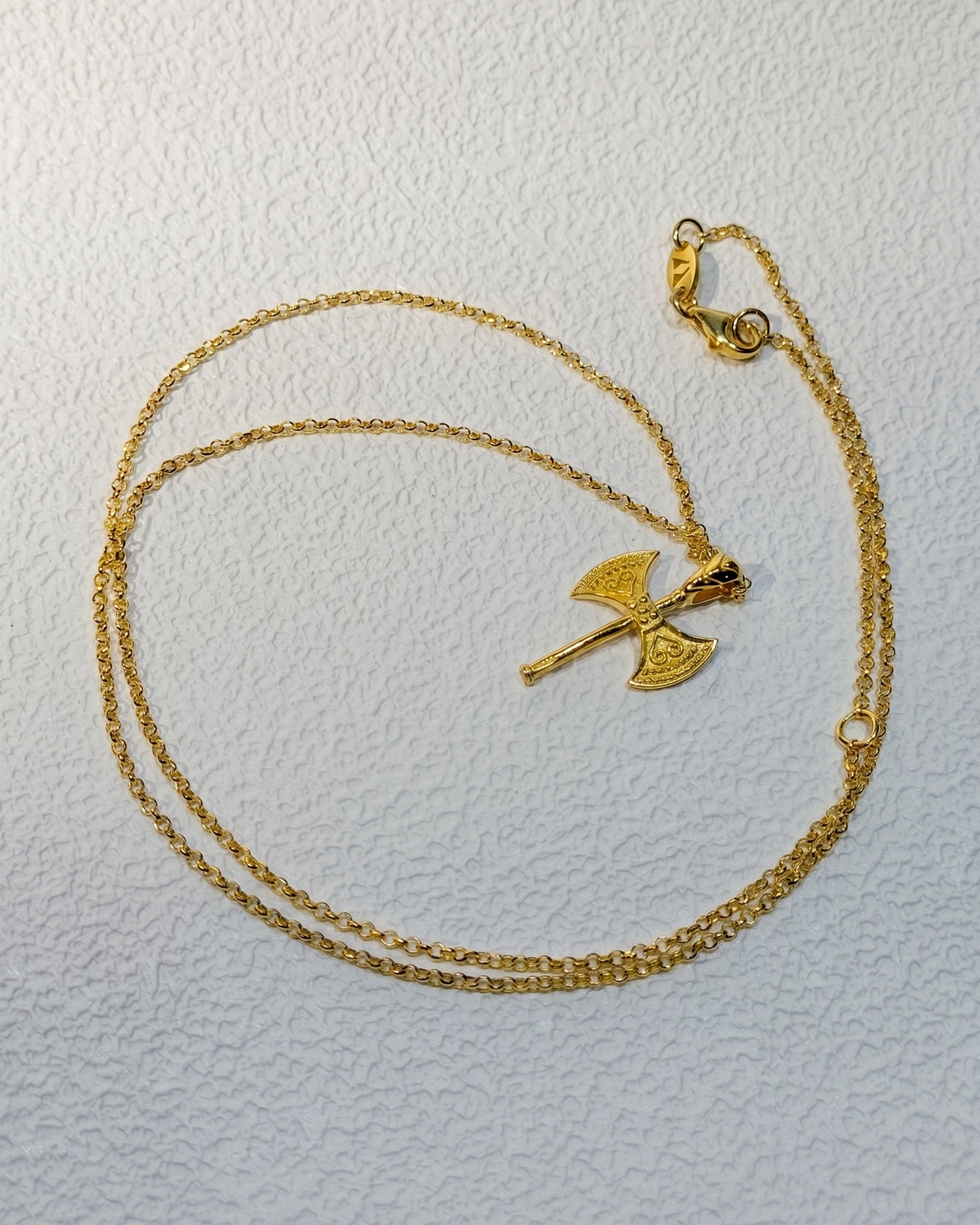 Gold necklace with a unique pendant on a light gray background