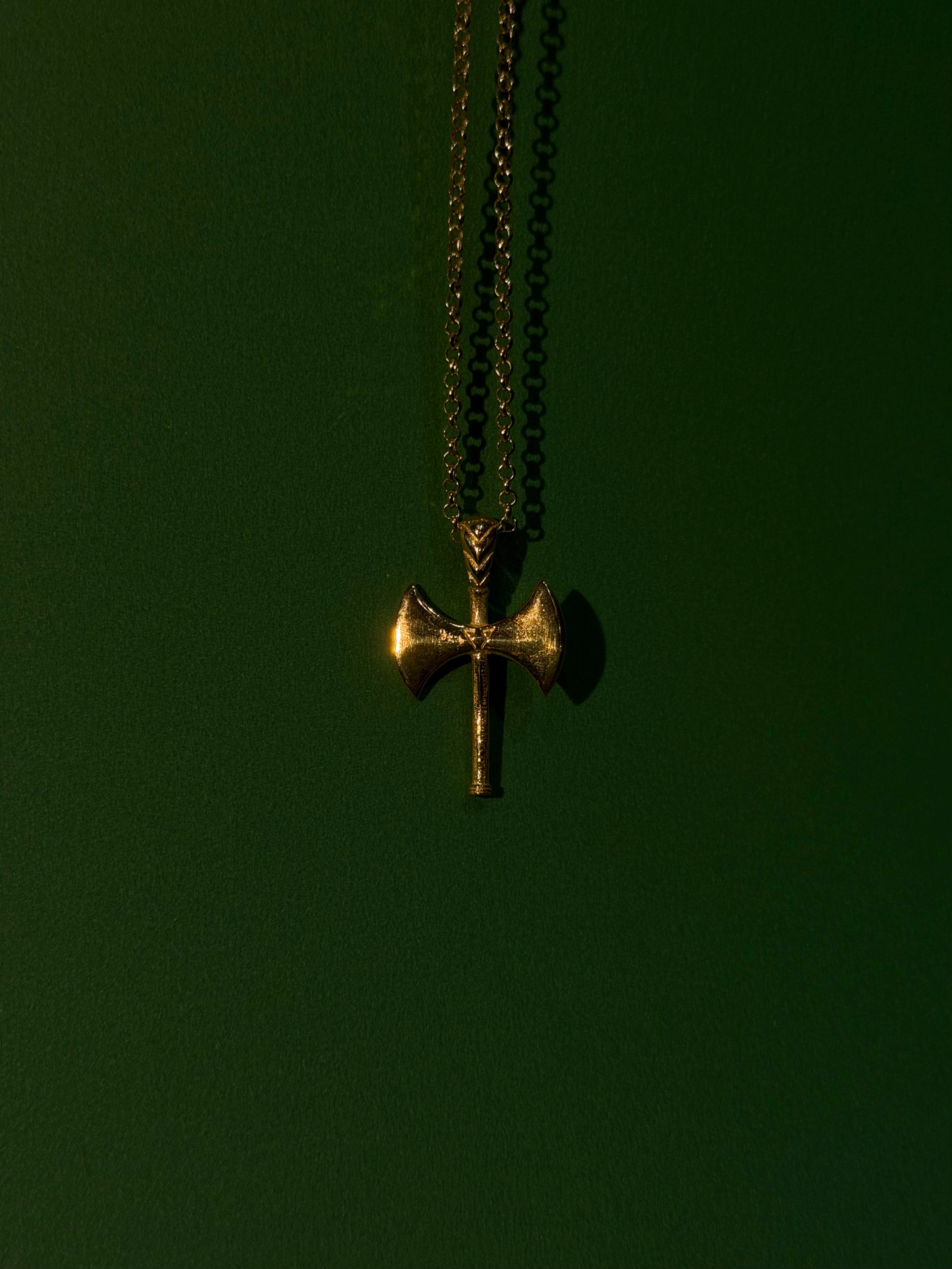 Gold cross pendant on a chain against a dark green background