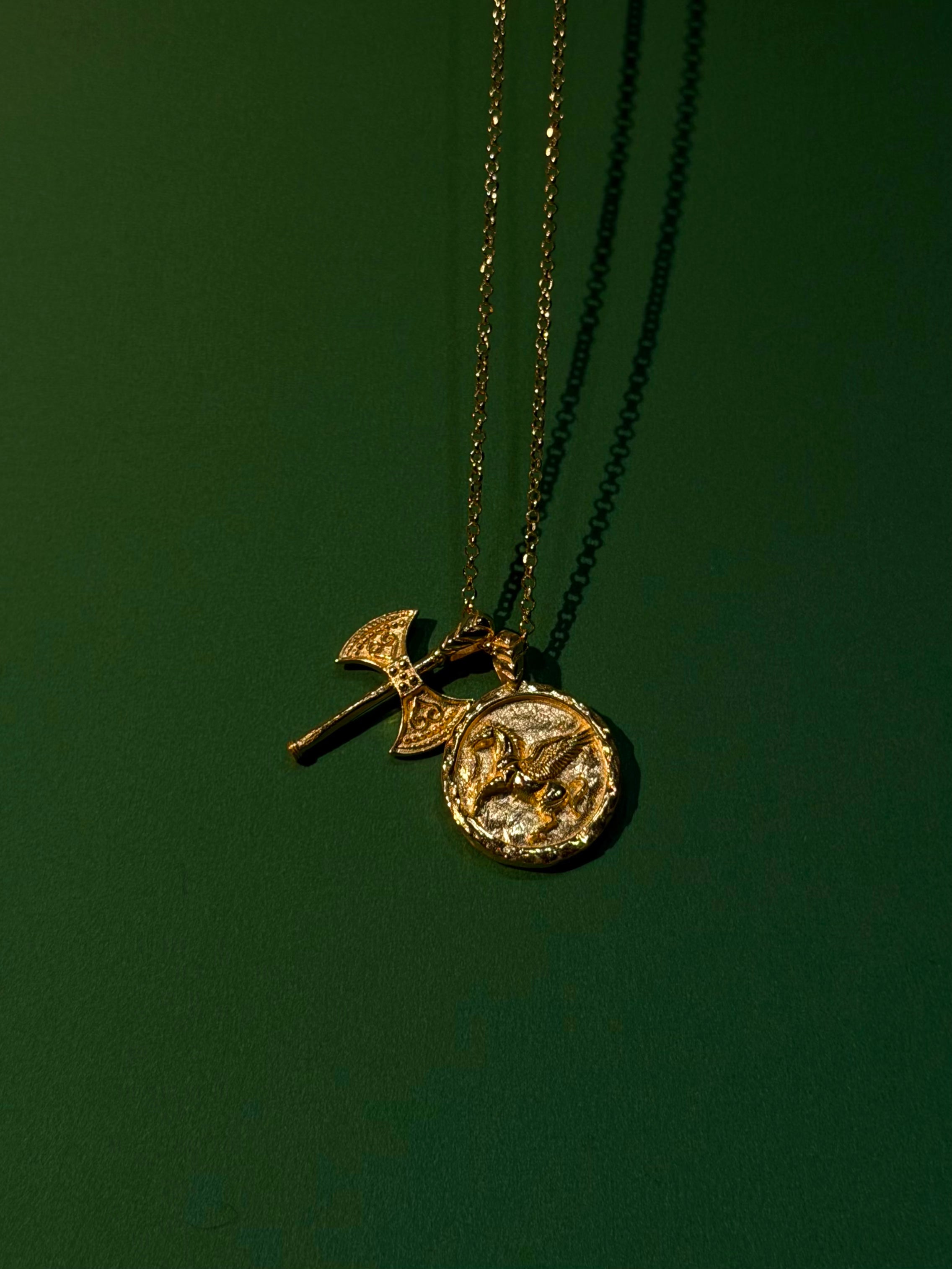 Gold necklace with two pendants on a dark green background