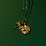 Gold necklace with two pendants on a green background