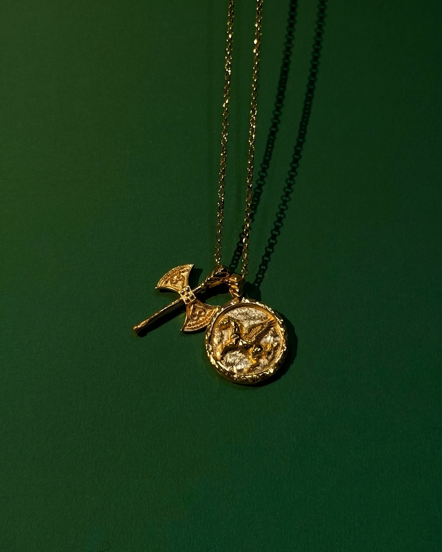 Gold necklace with two pendants on a green background