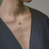 Close-up of a person wearing a necklace with a pendant against a neutral background
