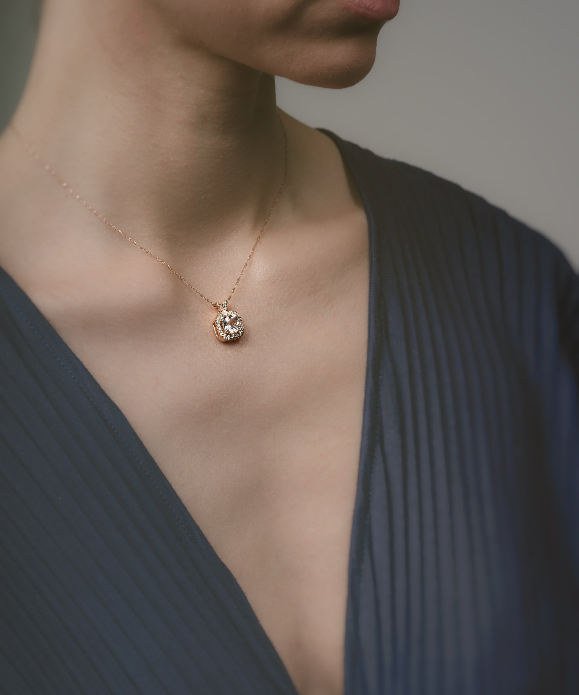 Close-up of a person wearing a necklace with a pendant against a neutral background