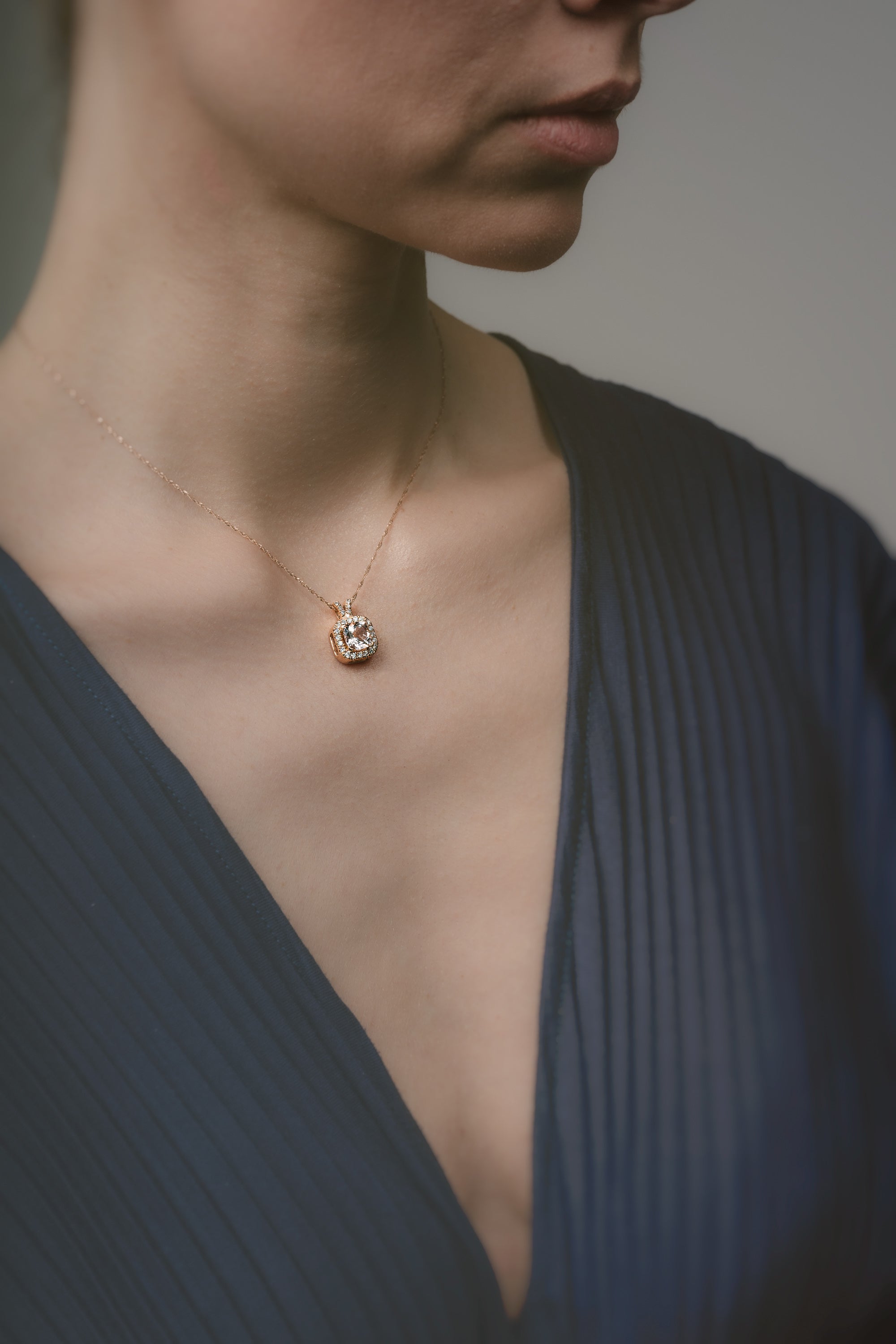 Close-up of a person wearing a necklace with a pendant against a neutral background