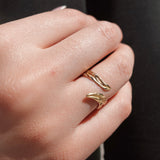 Close-up of a hand wearing an olive-shaped gold ring on a dark background