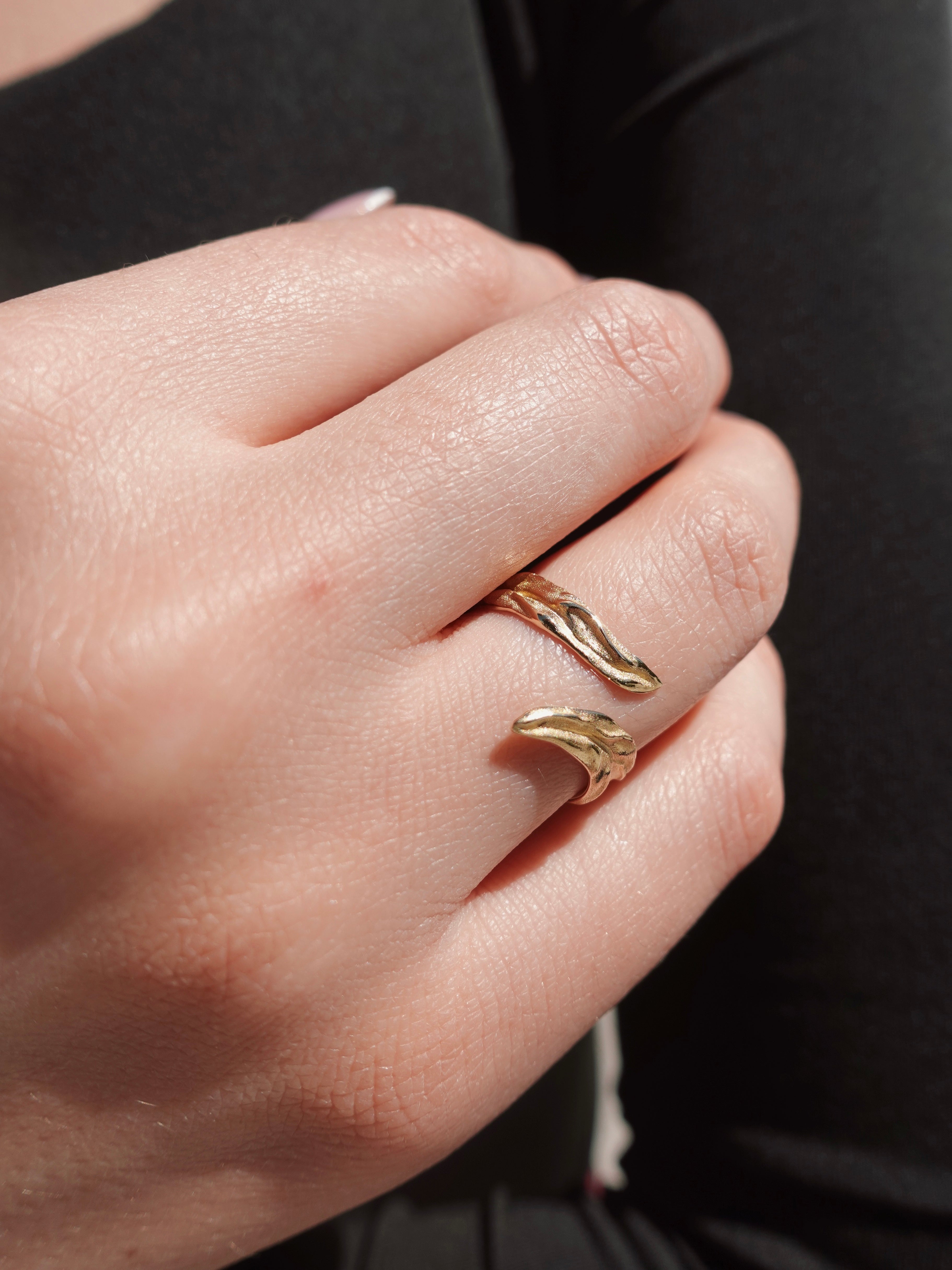 Close-up of a hand wearing an olive-shaped gold ring on a dark background