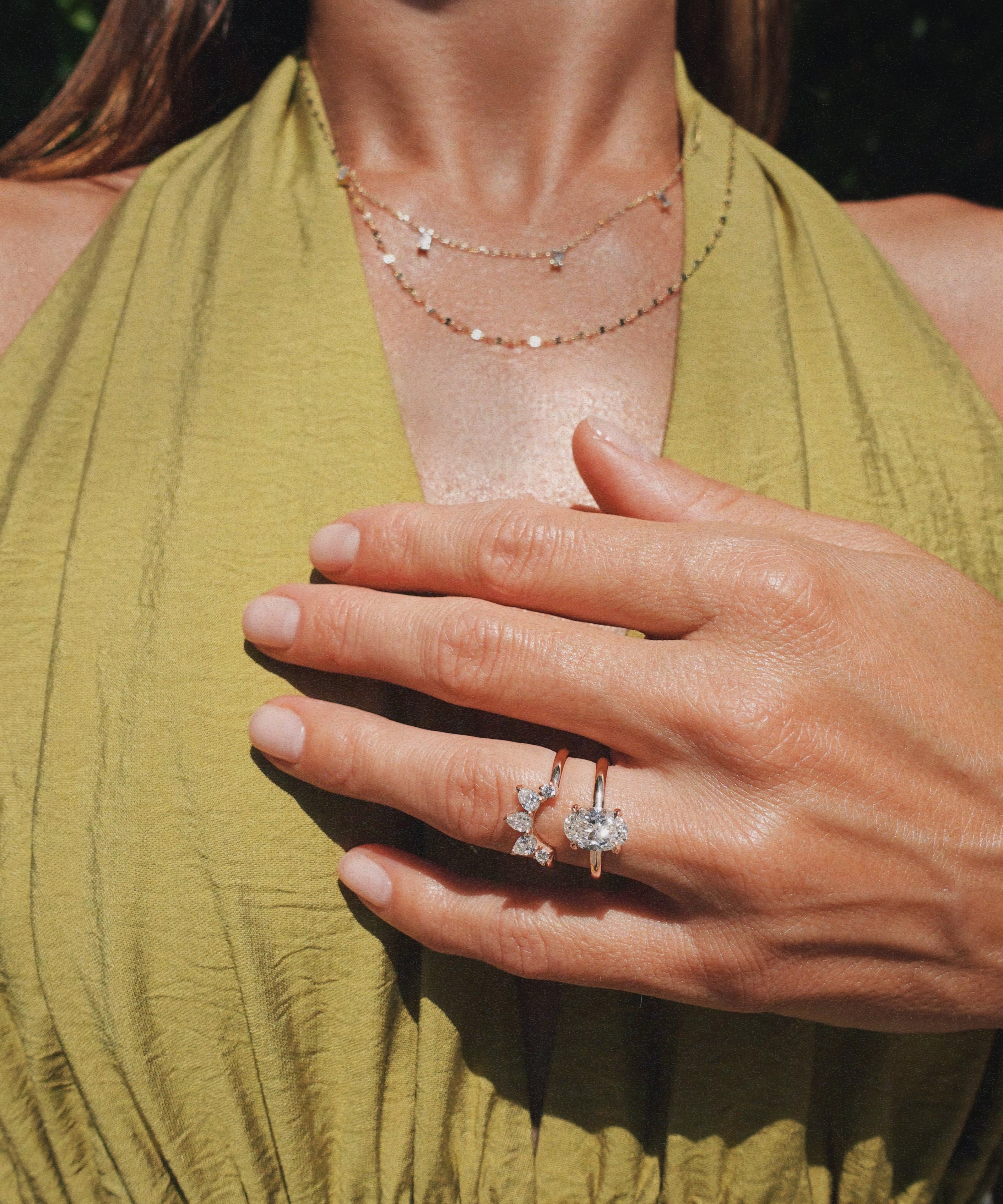 A close-up lifestyle shot of a woman wearing a delicate gold ring with a butterfly-shaped clear gemstone stack with another gold ring, paired with a green halter top.