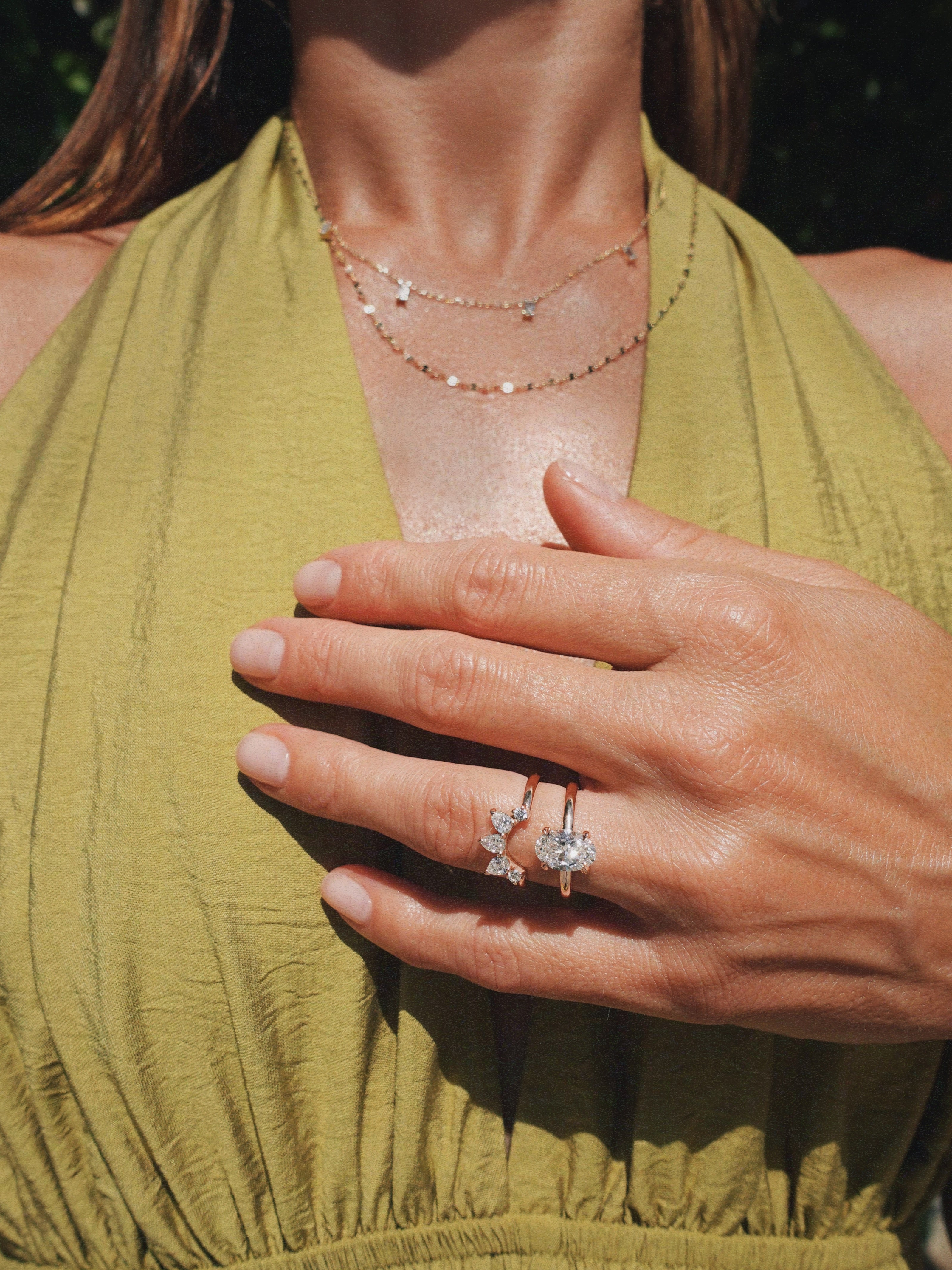 A close-up lifestyle shot of a woman wearing a delicate gold ring with a butterfly-shaped clear gemstone stack with another gold ring, paired with a green halter top.