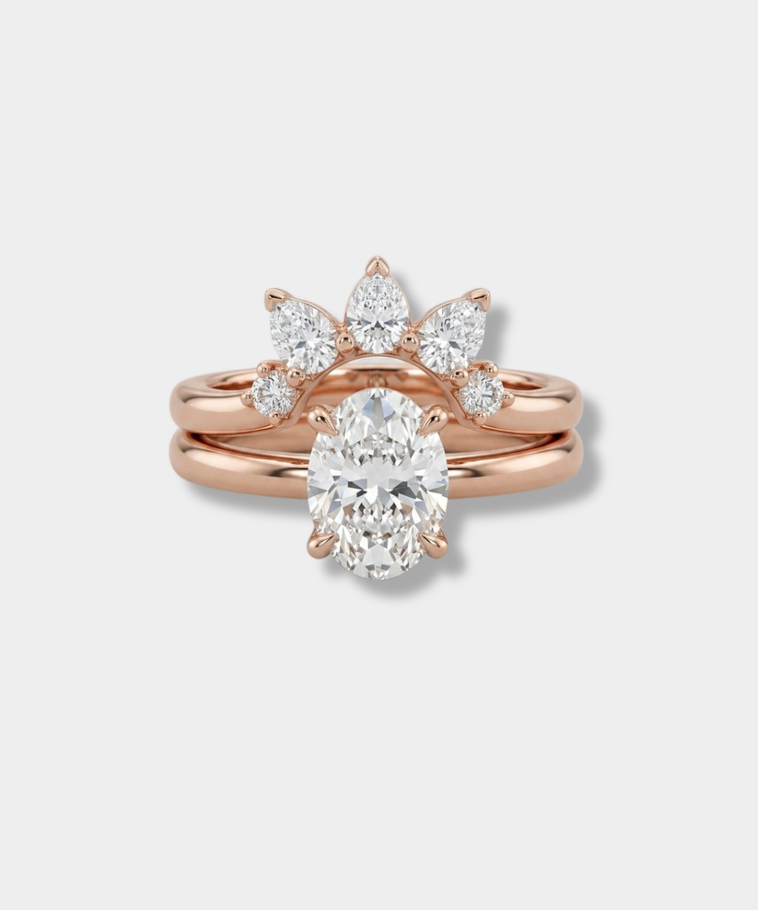 Rose gold wedding ring set featuring a central oval diamond solitaire ring with a matching three-stone sunburst cluster of pear, round, and marquise diamonds on a matching rose gold band, shown on a light gray background.