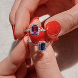 Two rings with gemstones held between fingers against a neutral background