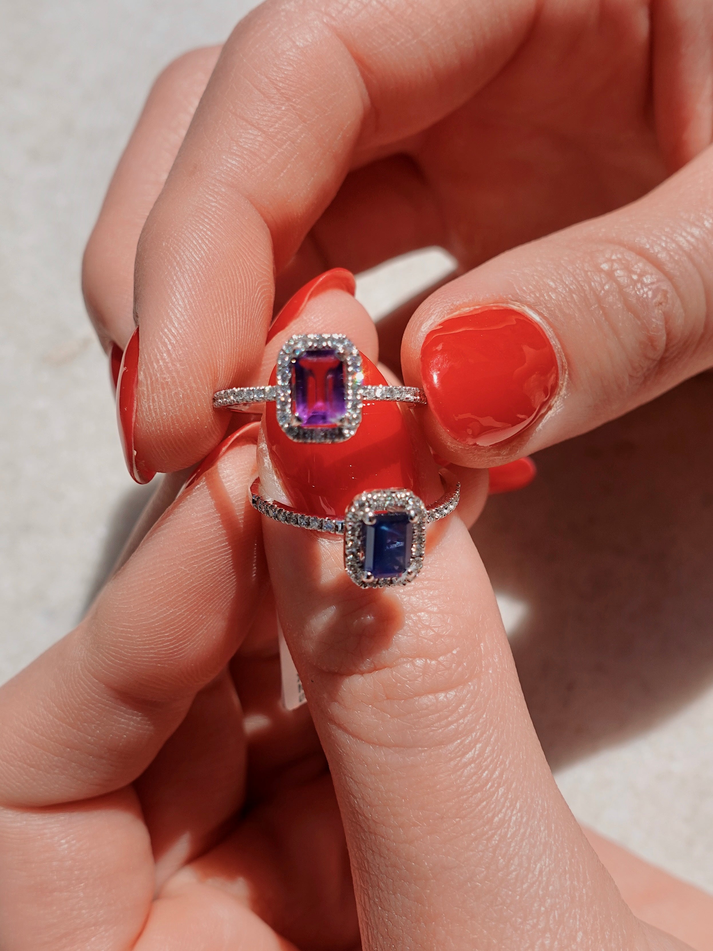 Two rings with gemstones held between fingers against a neutral background