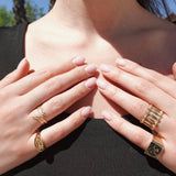 Close-up of hands wearing gold rings with a blurred outdoor background