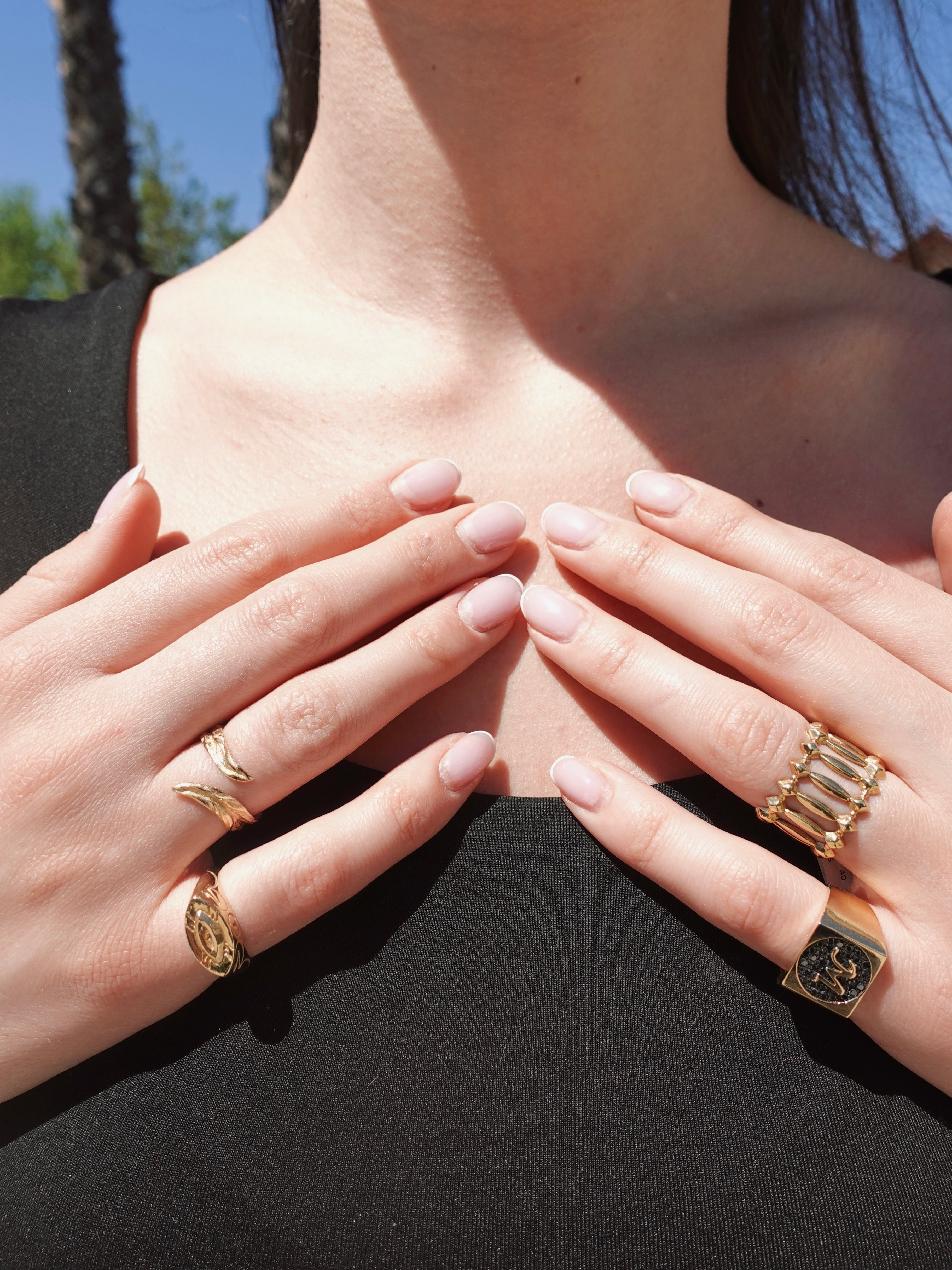 Close-up of hands wearing gold rings with a blurred outdoor background