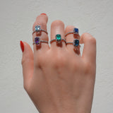 Hand wearing multiple rings with gemstones on a plain background