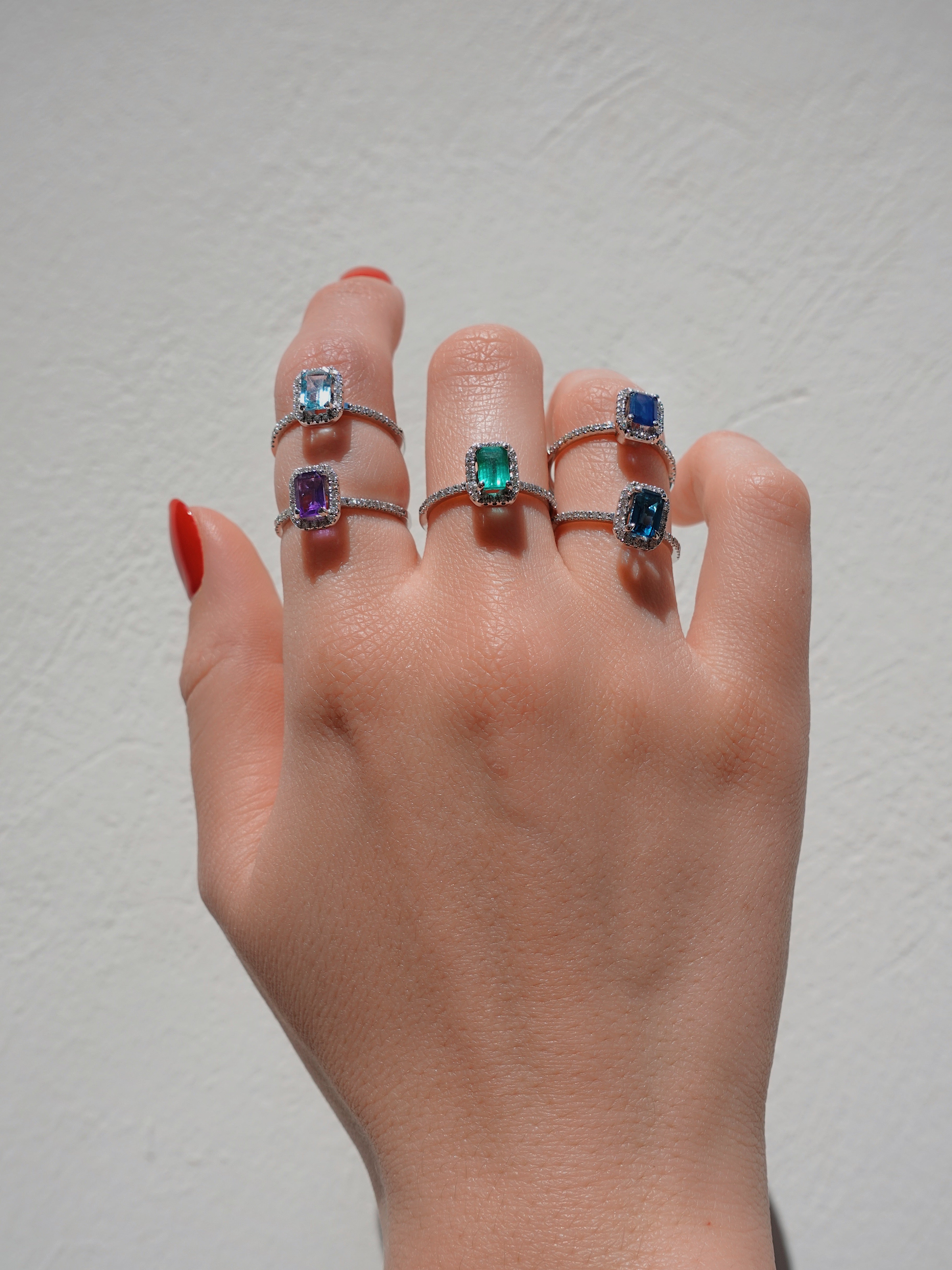 Hand wearing multiple rings with gemstones on a plain background
