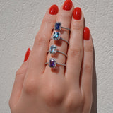 Hand wearing three rings with gemstones on a neutral background