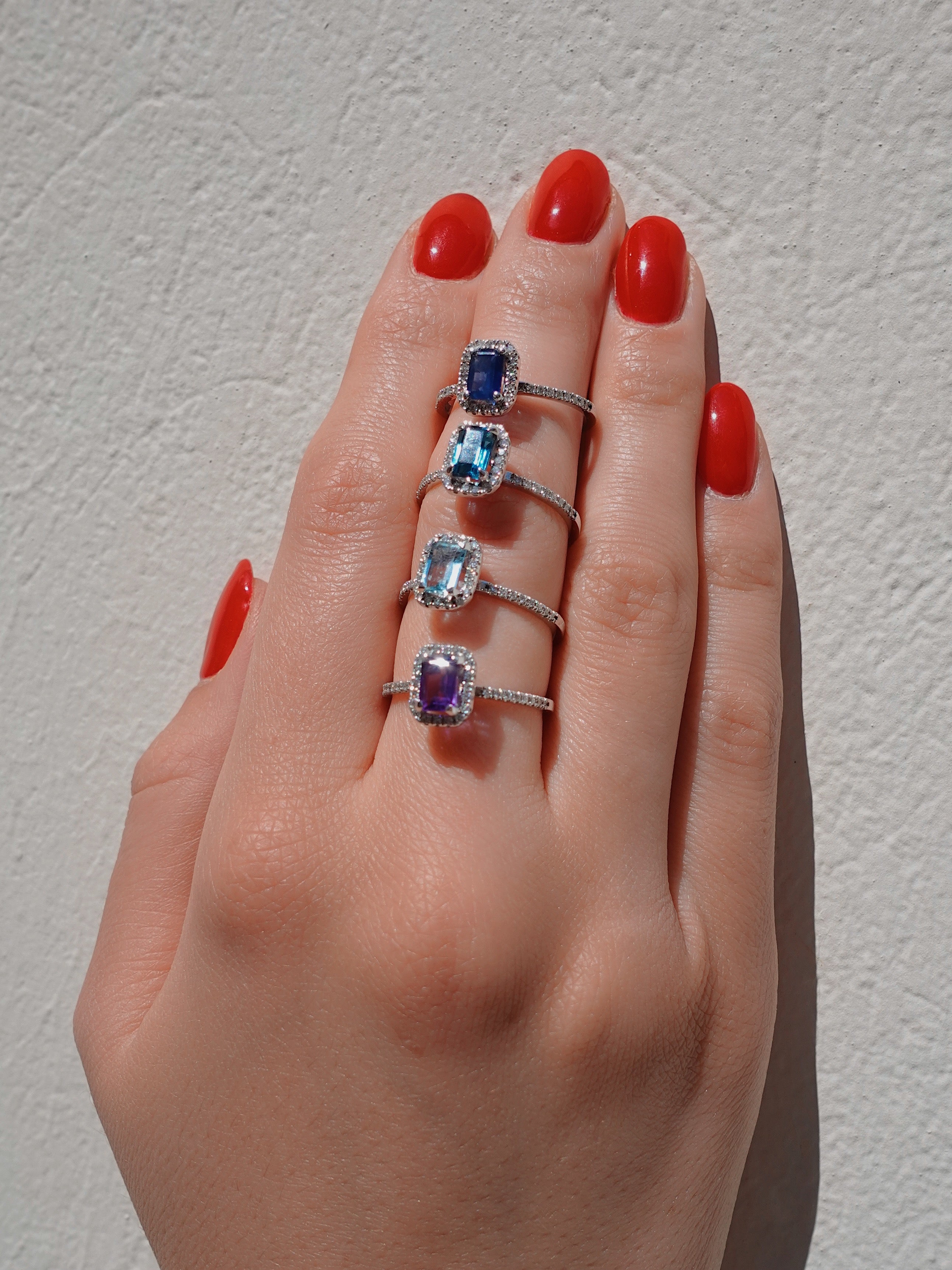 Hand wearing three rings with gemstones on a neutral background