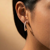 Close-up of an ear wearing a rose gold crossover hoop earring with a neutral background