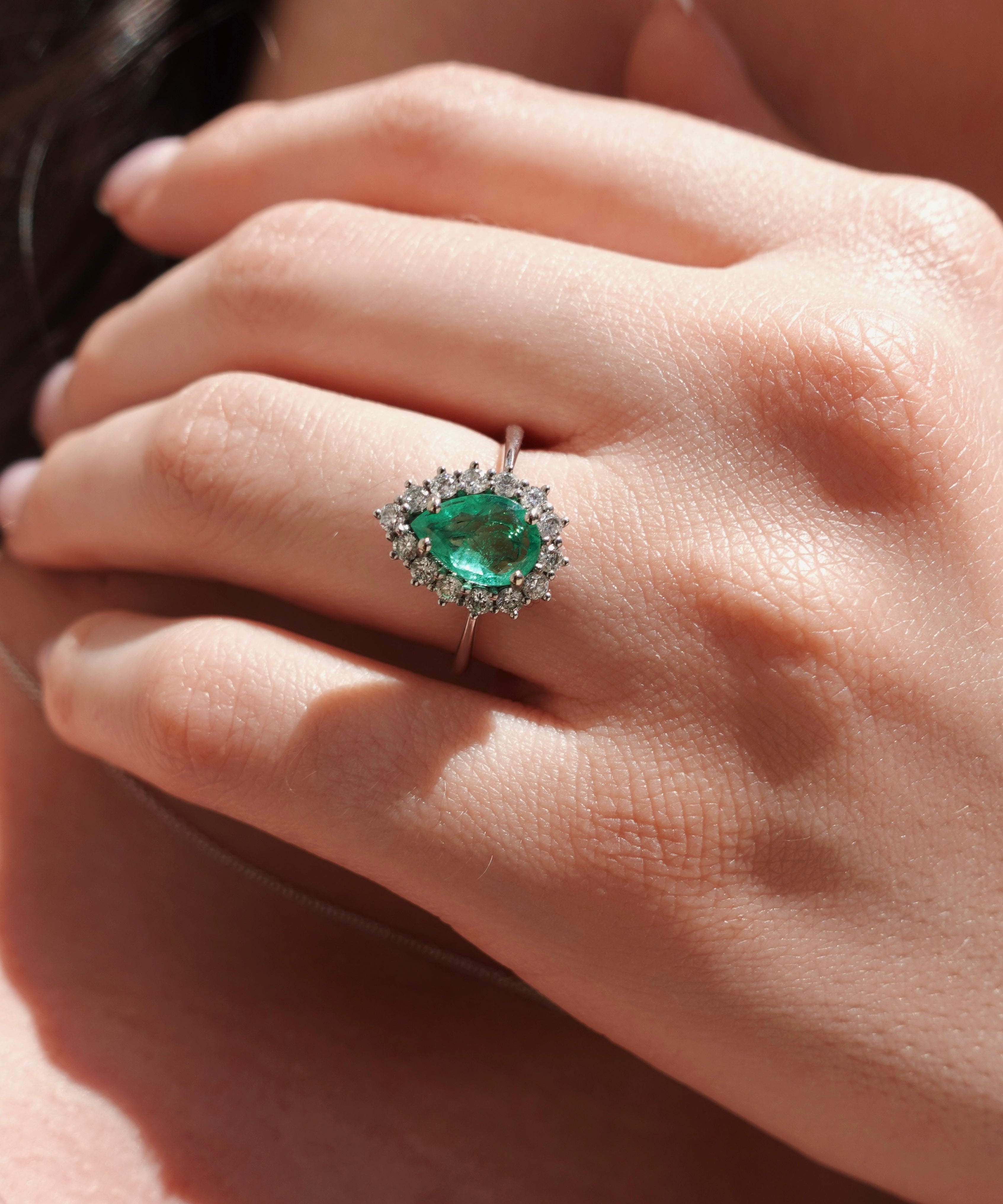 Close-up of a hand wearing an emerald ring with a blurred background