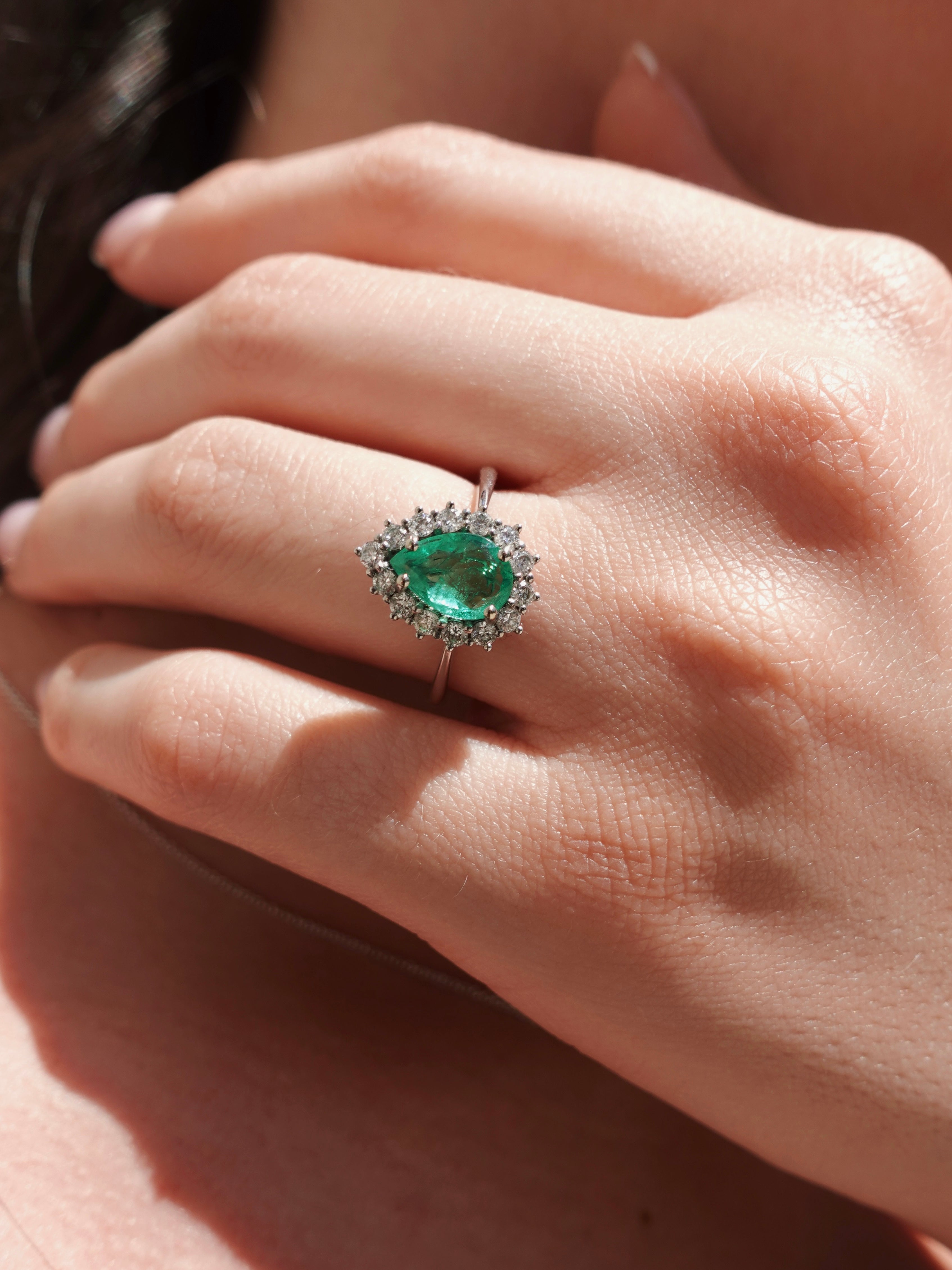 Close-up of a hand wearing an emerald ring with a blurred background