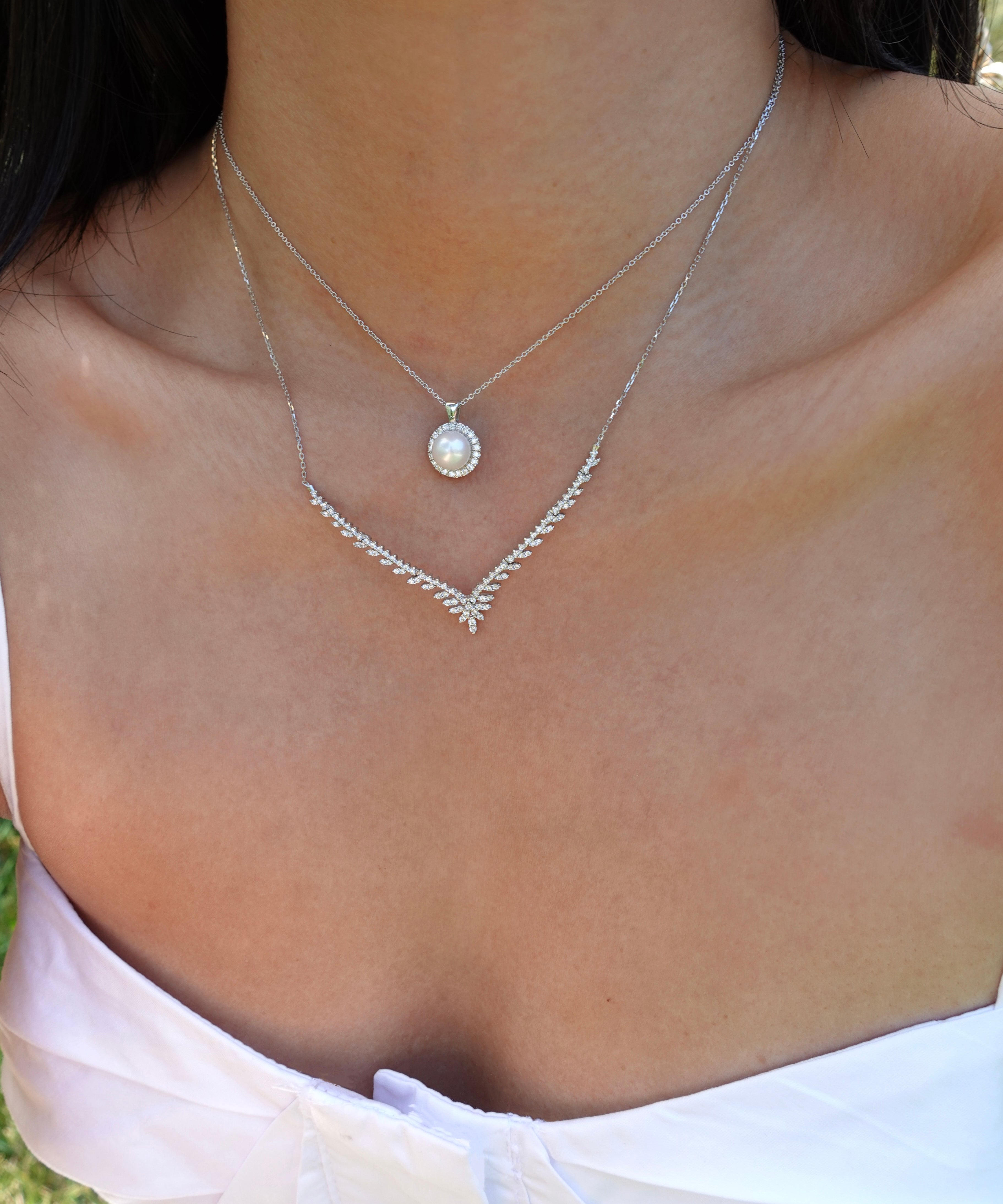Close-up of a necklace with a pearl pendant on a person wearing a white top.