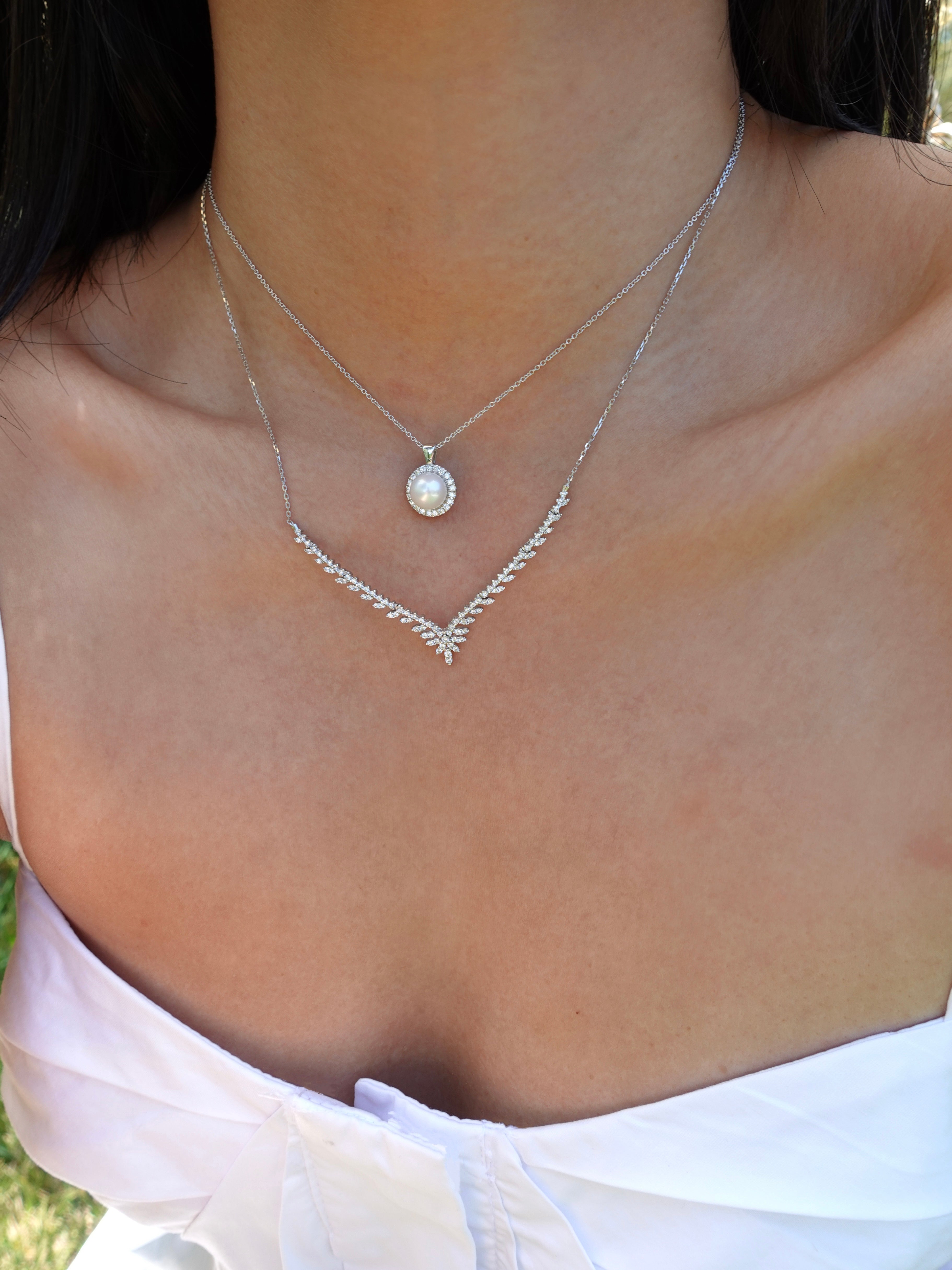 Close-up of a necklace with a pearl pendant on a person wearing a white top.