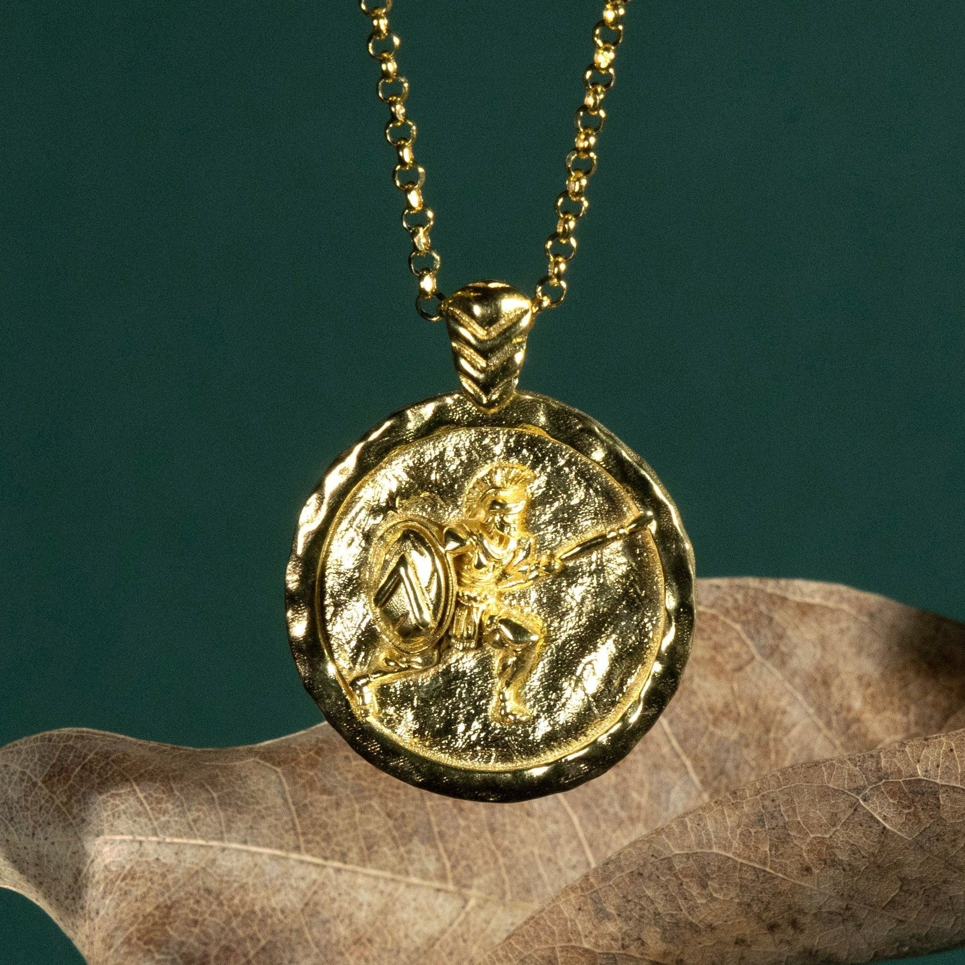 Gold necklace with a coin pendant featuring a Spartan soldier on a dark green background