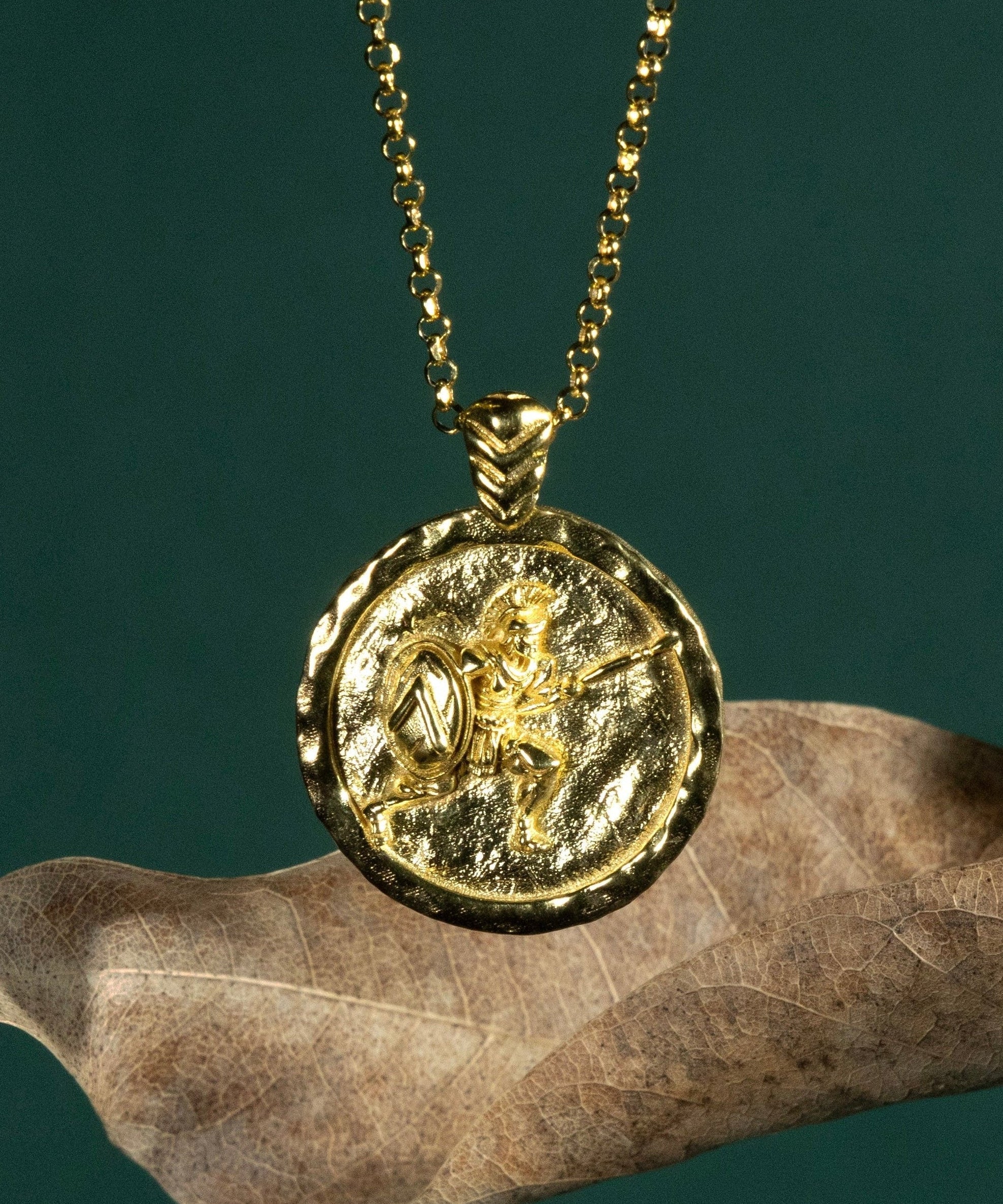 Gold necklace with a coin pendant featuring a Spartan soldier on a dark green background