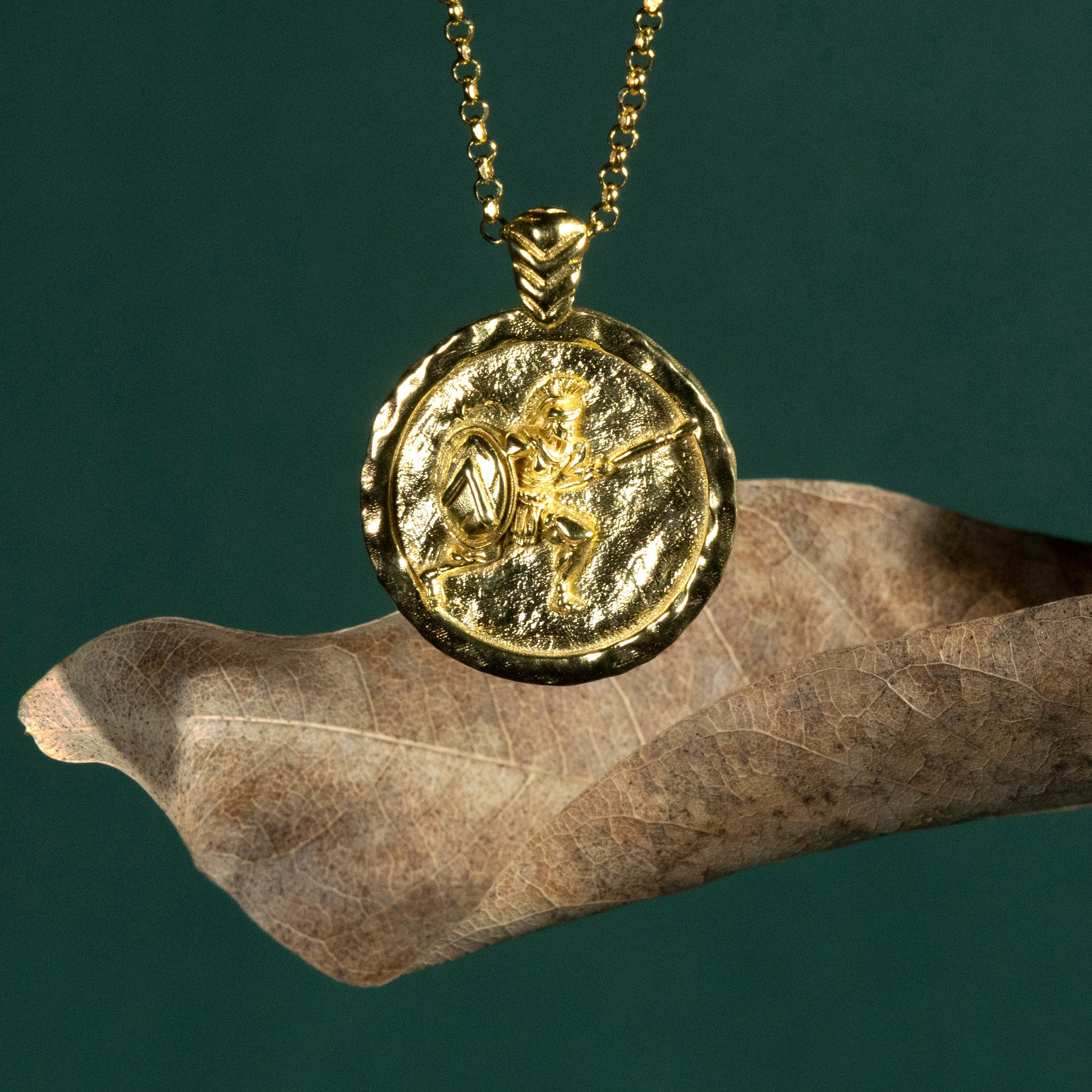Gold necklace with a coin pendant featuring a Spartan soldier on a dark green background