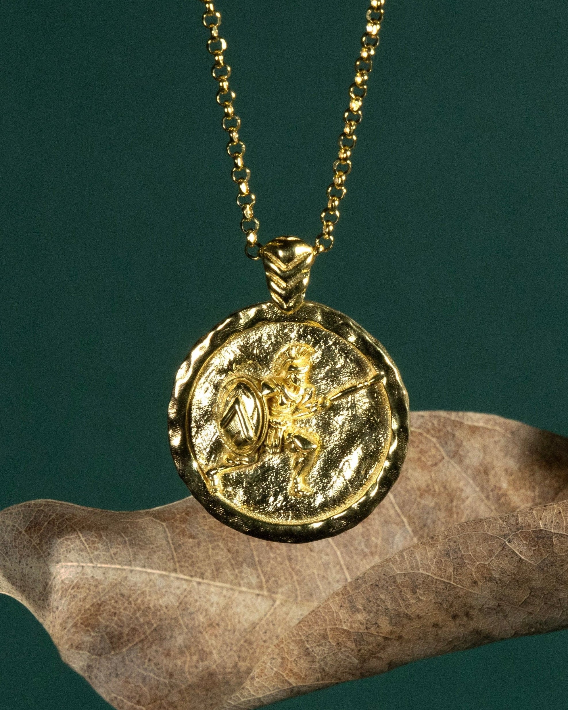 Gold necklace with a coin pendant featuring a Spartan soldier on a dark green background