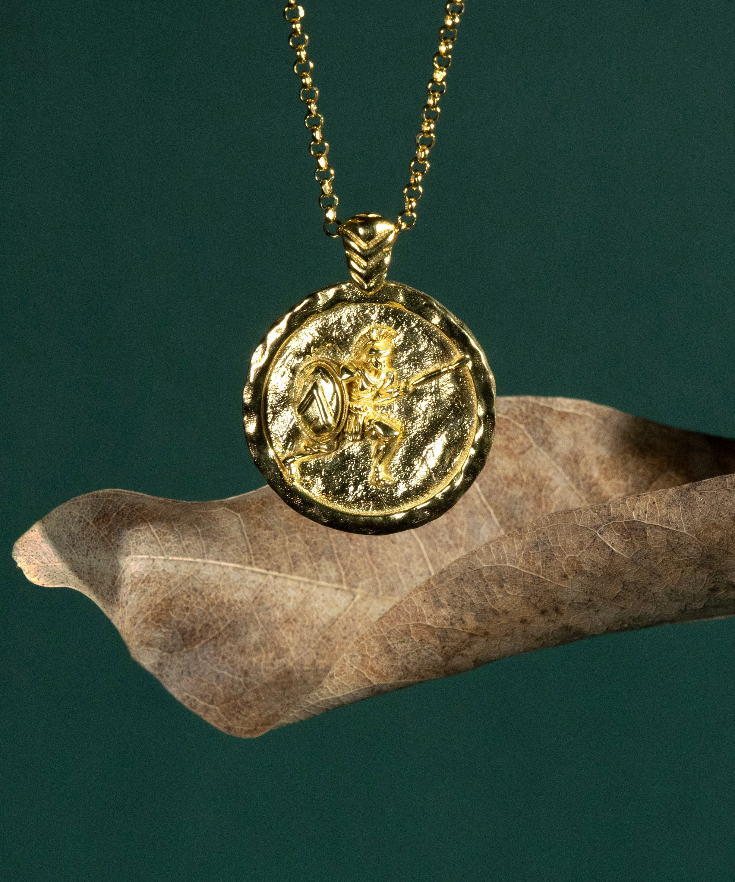 Gold necklace with a coin pendant featuring a Spartan soldier on a dark green background