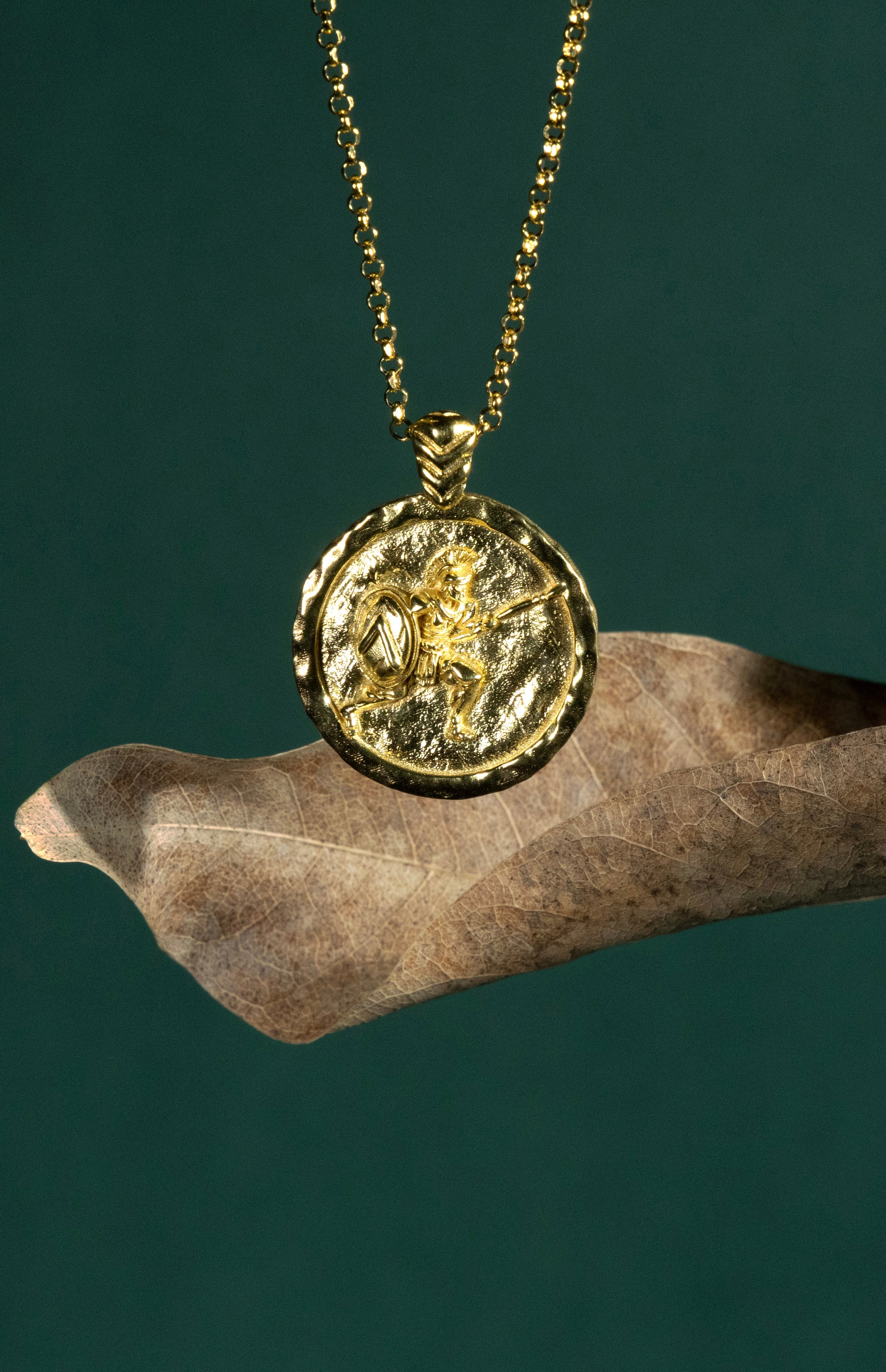 Gold necklace with a coin pendant featuring a Spartan soldier on a dark green background