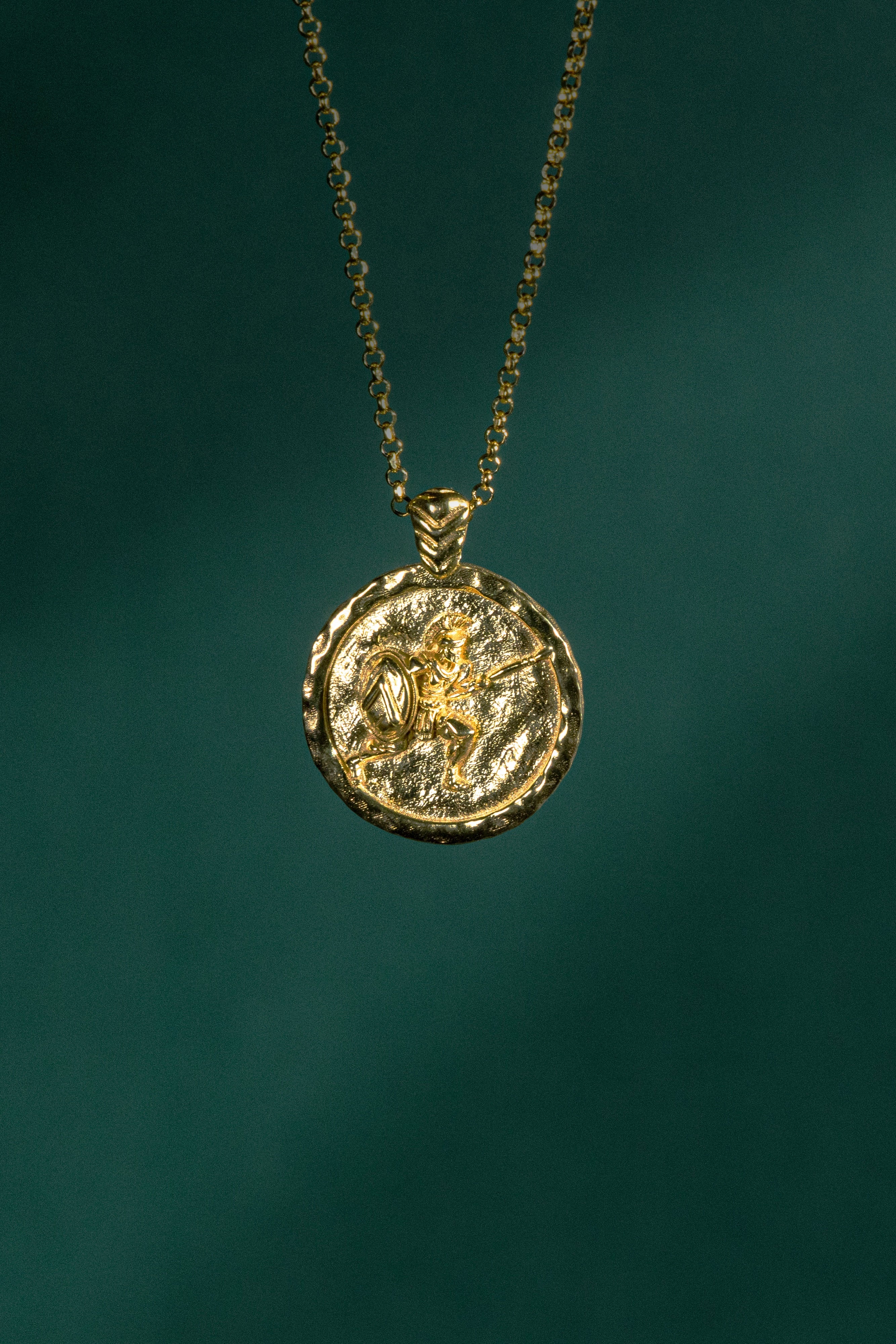 Gold necklace with a round pendant on a dark green background