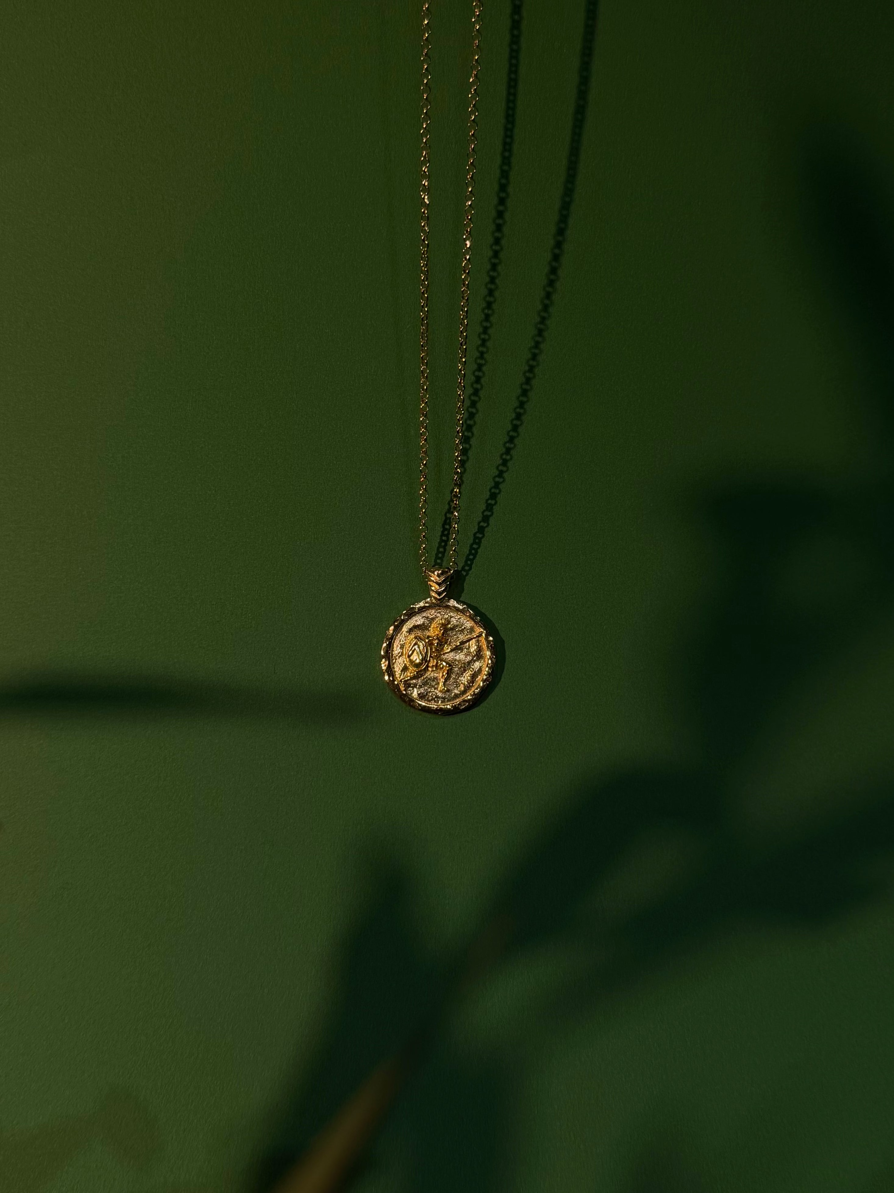 Gold necklace with a circular pendant featuring a Spartan soldier on a dark green background