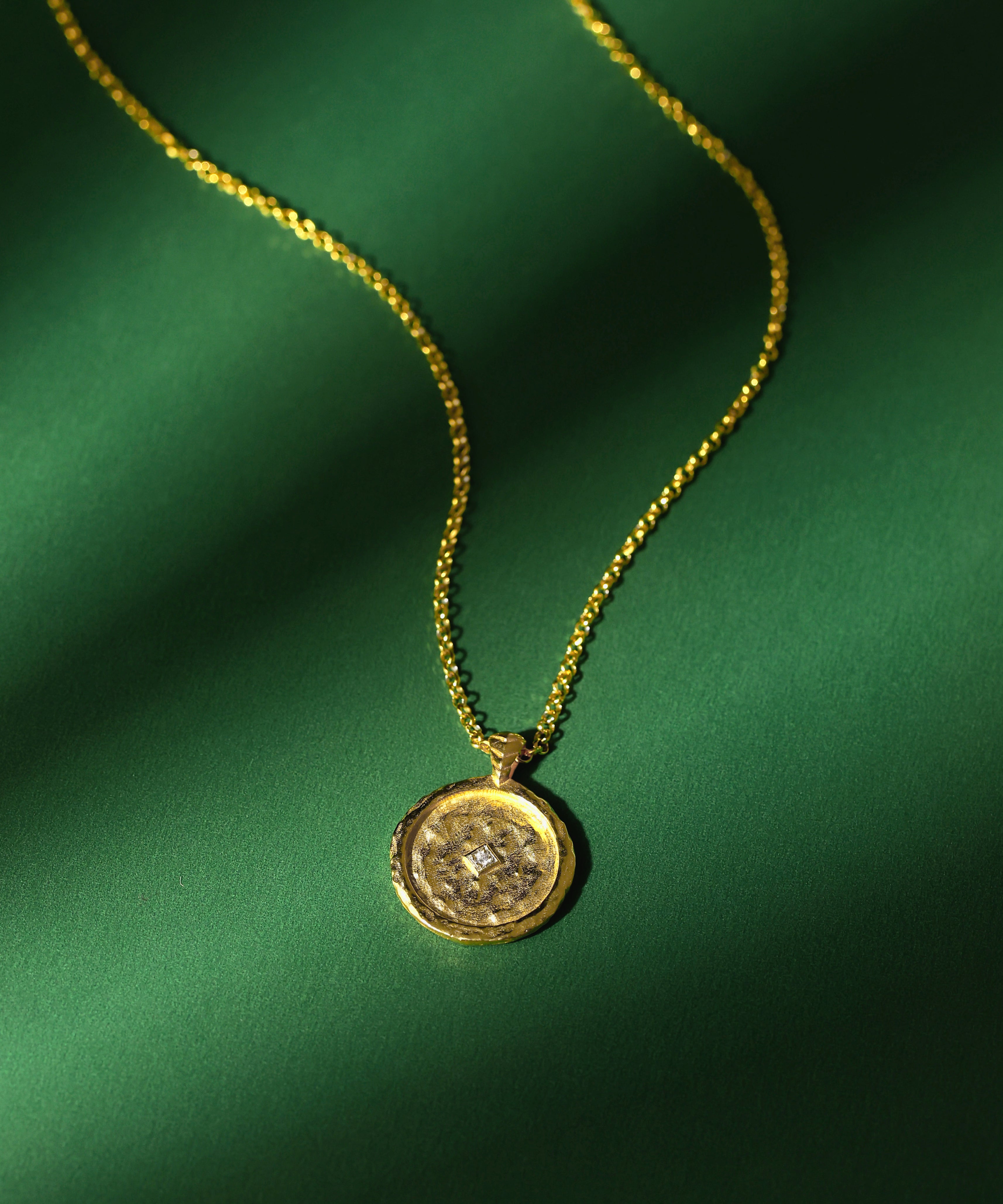 Gold necklace with a pendant and a zircon on a green fabric background