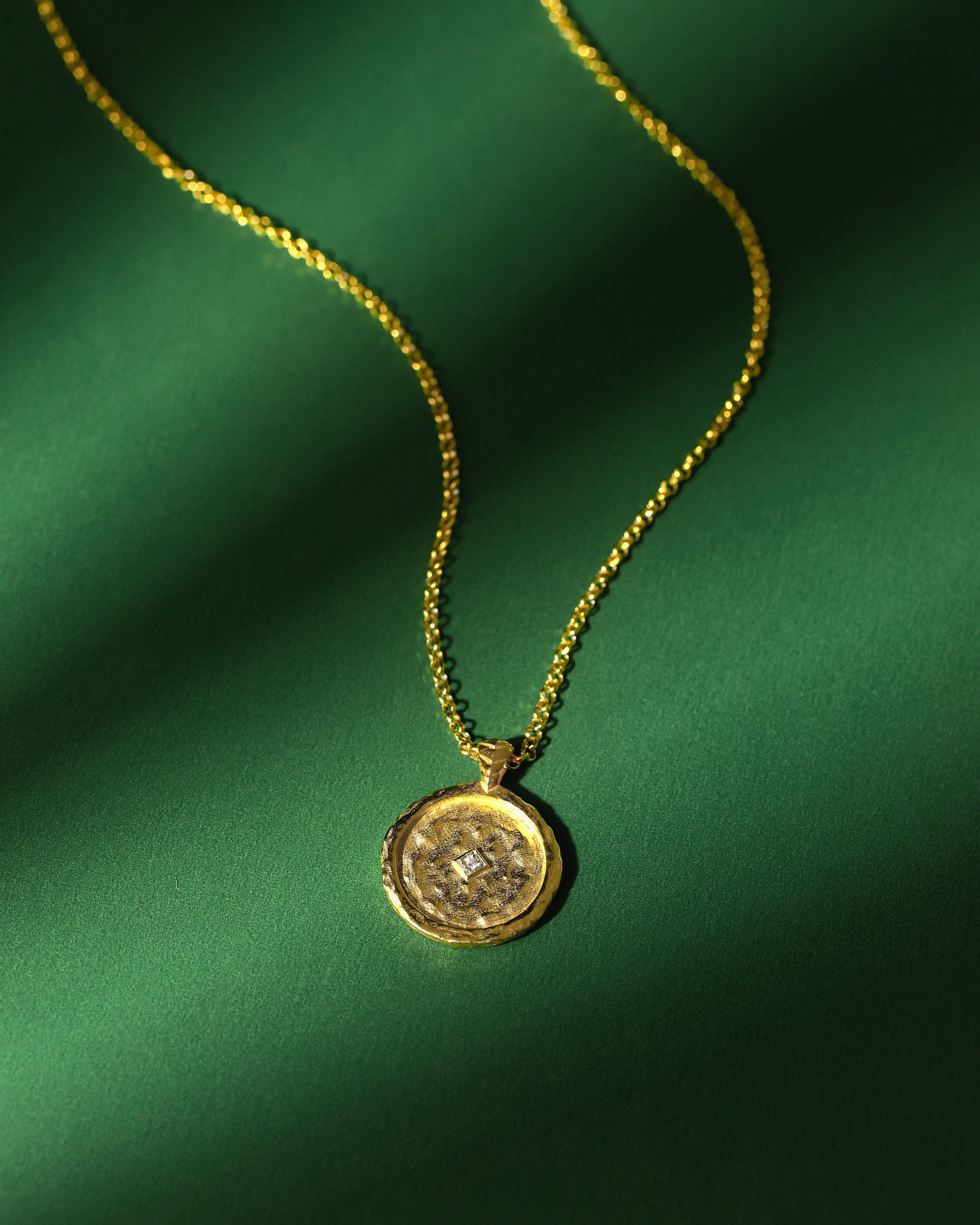 Gold necklace with a pendant and a zircon on a green fabric background