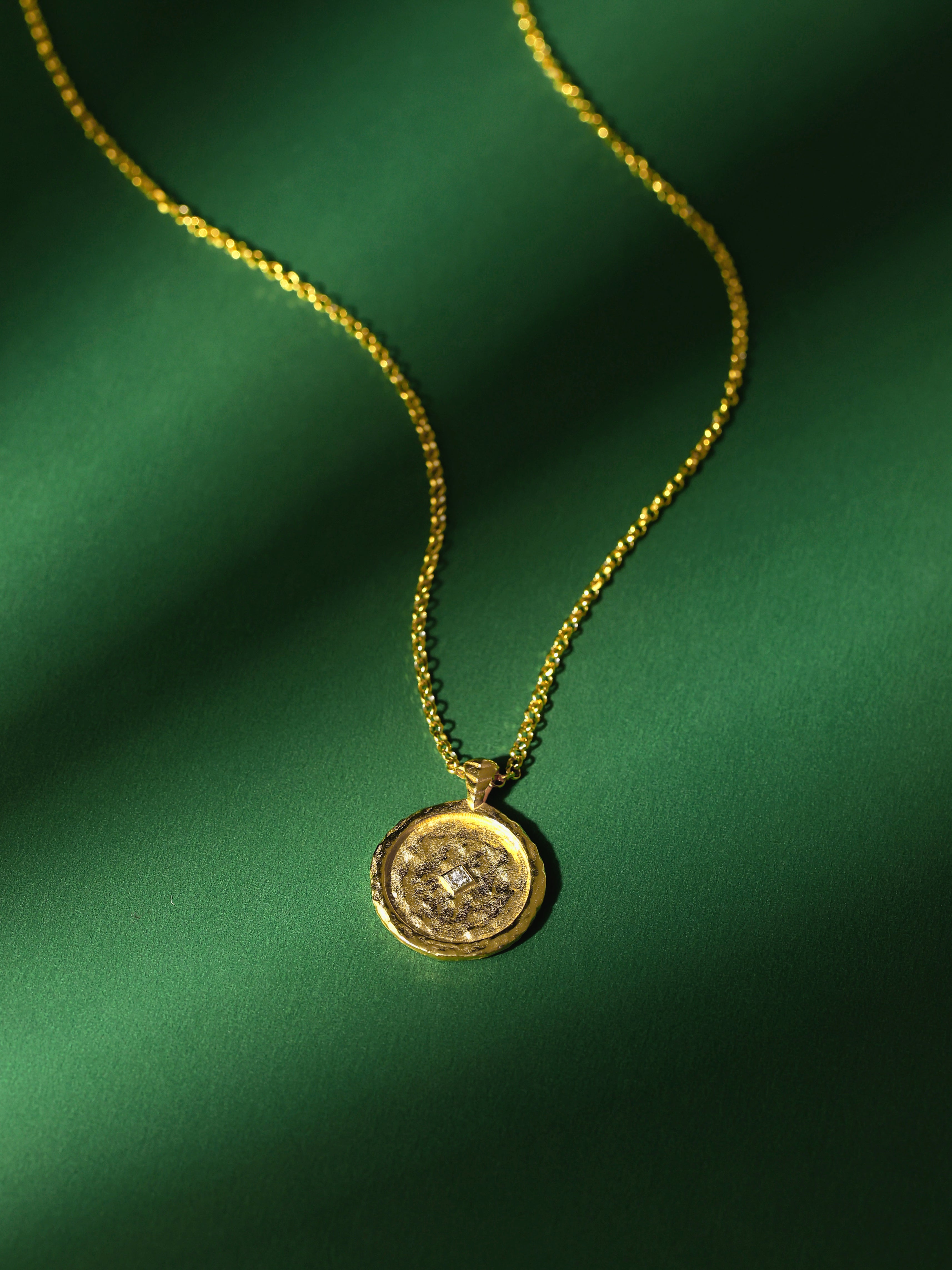 Gold necklace with a pendant and a zircon on a green fabric background
