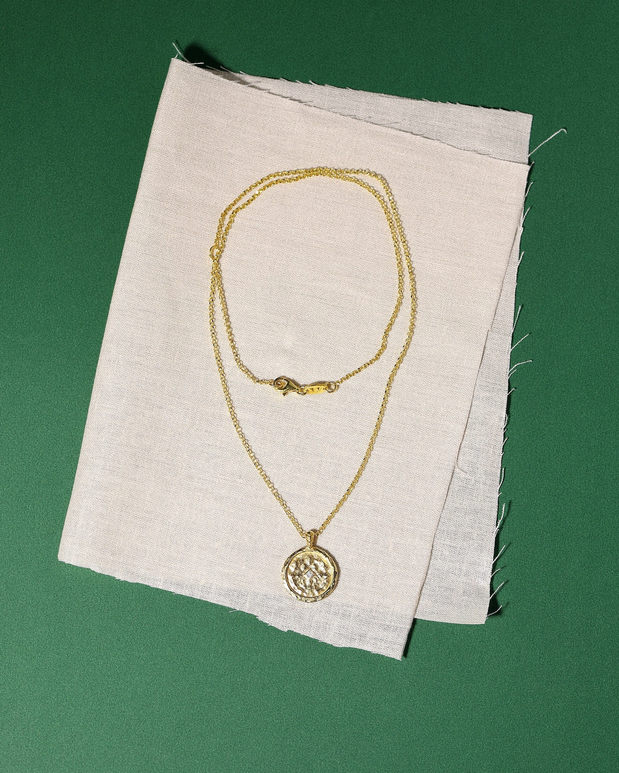 Gold necklace with a pendant and a zircon on a white fabric background