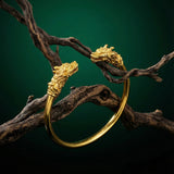 Gold bracelet with dragon head designs on a dark background