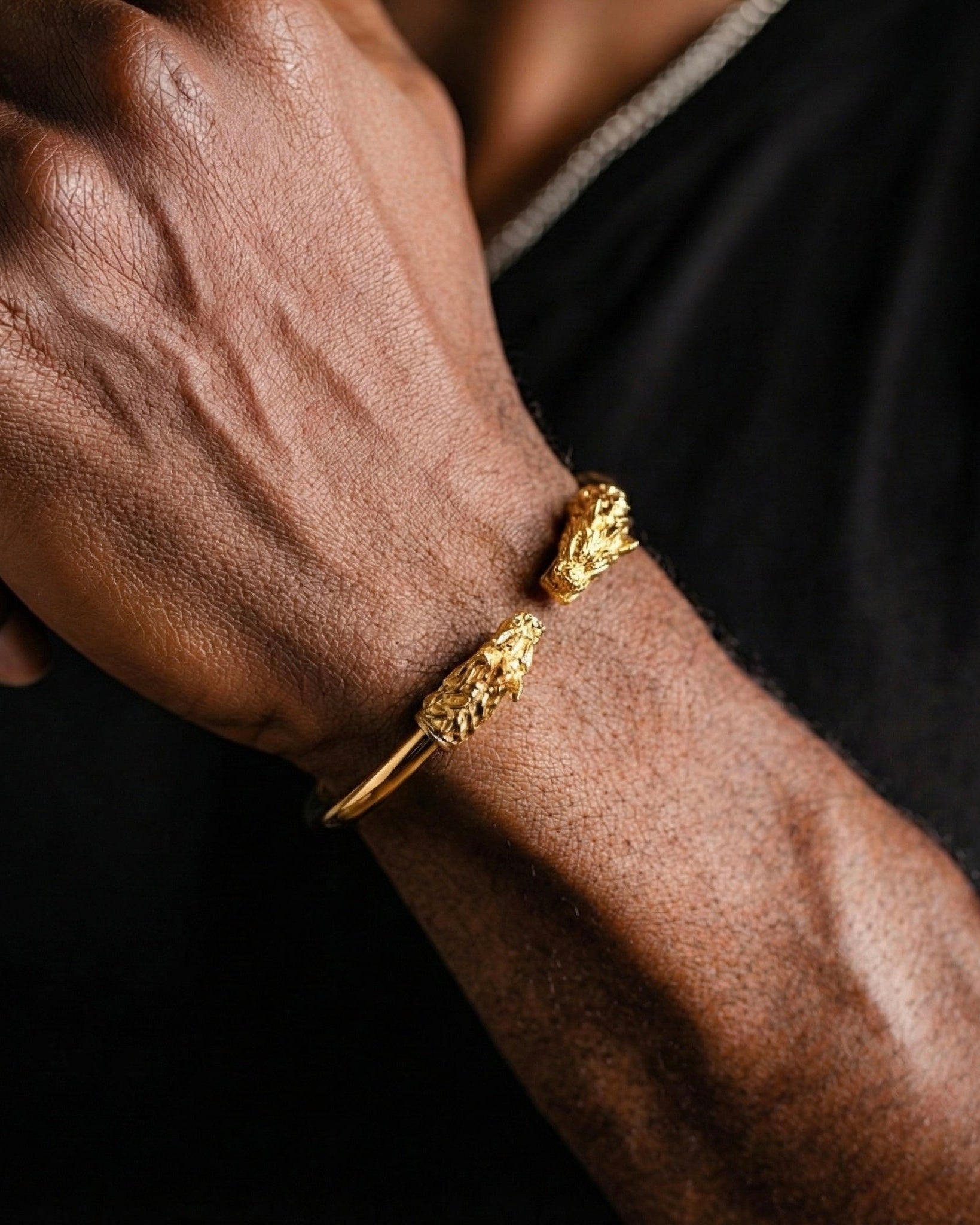 Close-up of a person's arm wearing two gold bracelets on a dark background