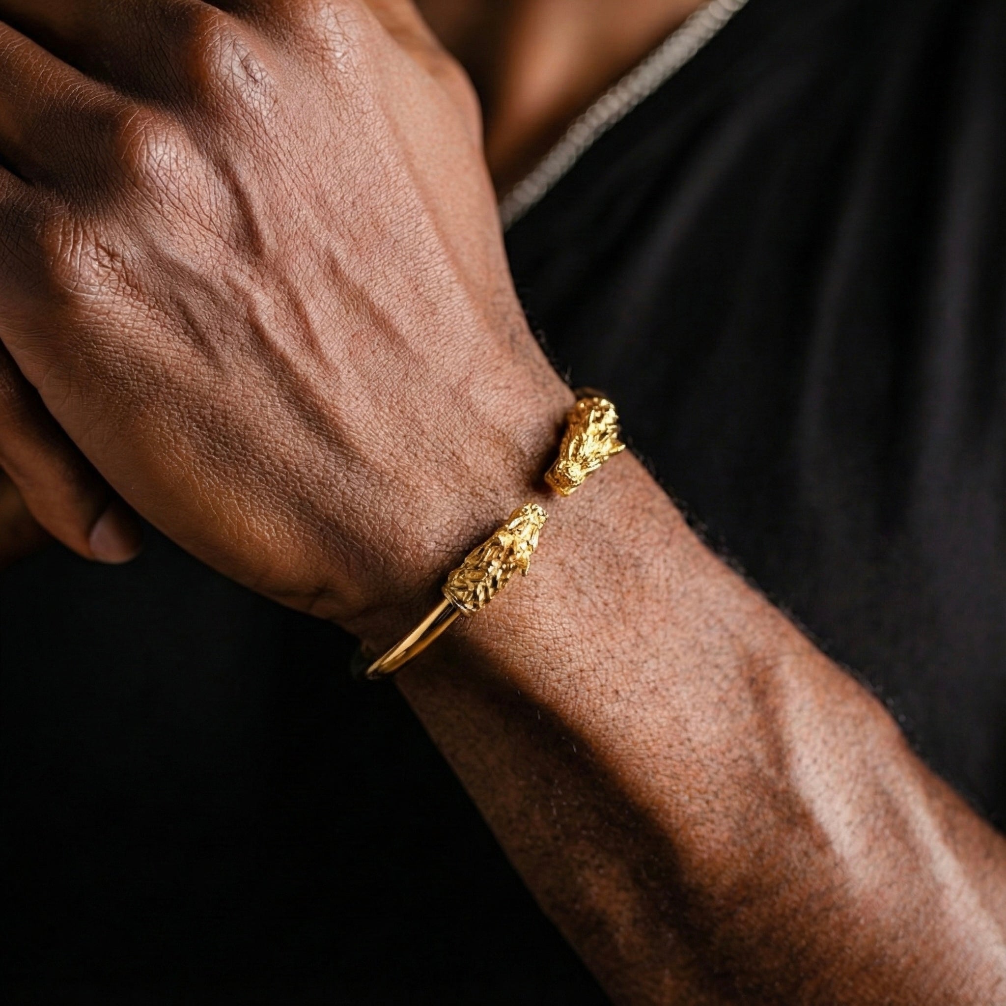 Close-up of a person's arm wearing two gold bracelets on a dark background