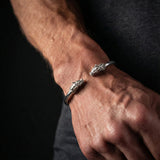 Close-up of a person's wrist wearing two silver bracelets on a dark background