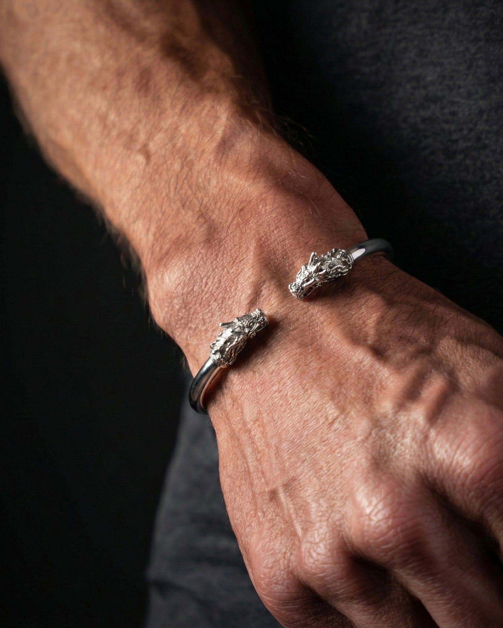 Close-up of a person's wrist wearing two silver bracelets on a dark background