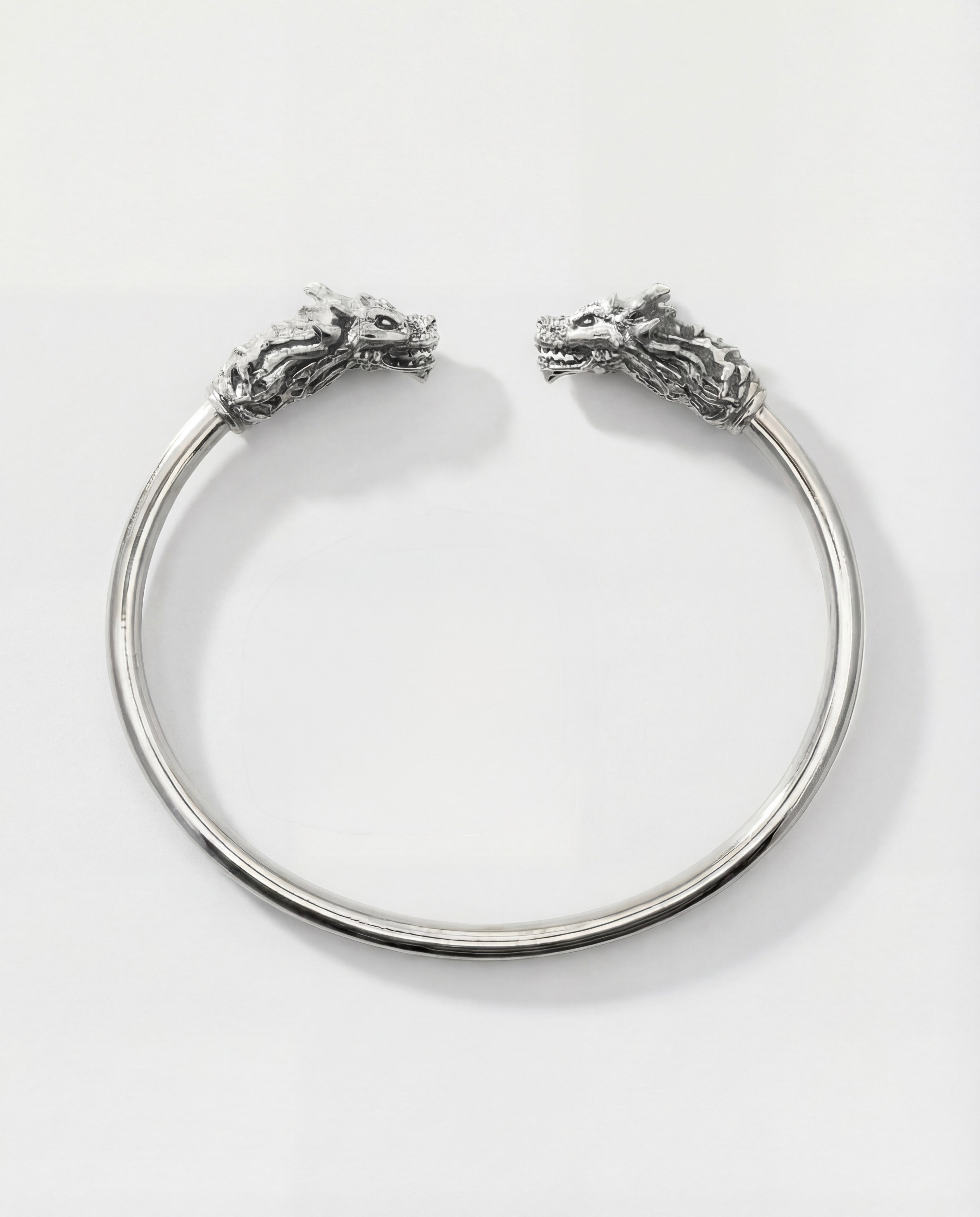 Silver bracelet with dragon head designs on a white background